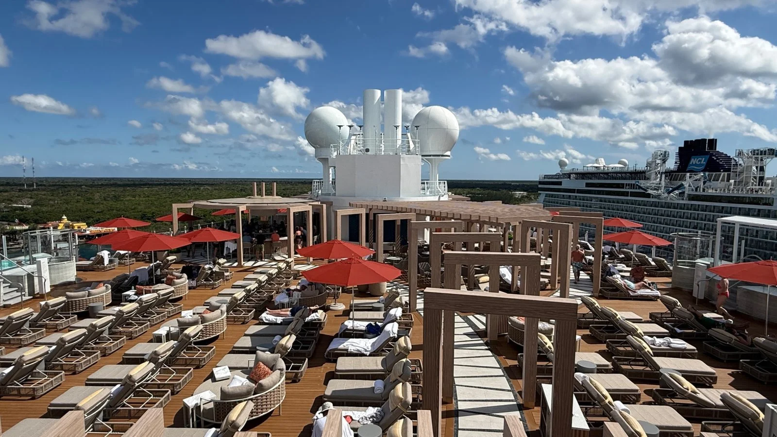 Cruise ship sundeck with sun loungers, cabanas and ocean views under a bright blue sky