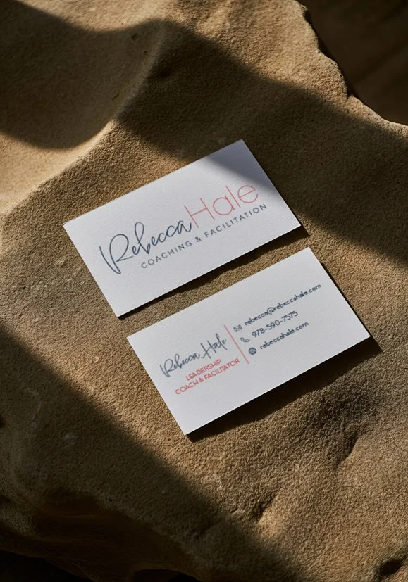 Two business cards for Rebecca Hale, a coaching and facilitation leader, placed on sandy surface with shadows.