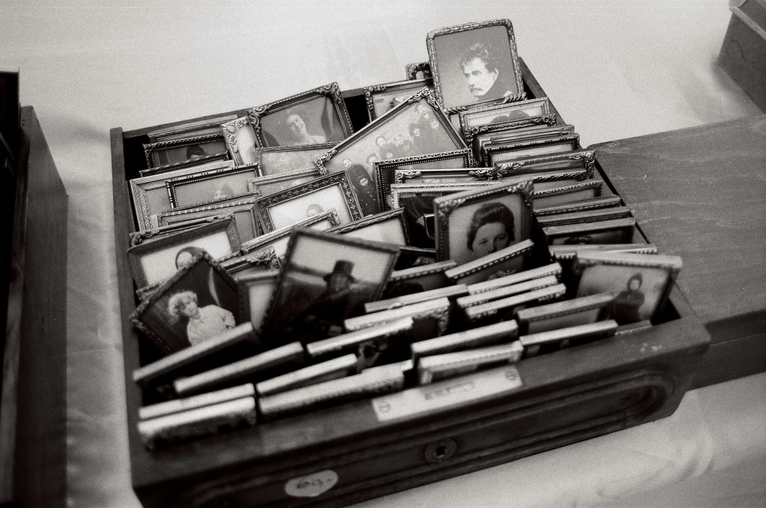 A wooden box filled with numerous small framed black-and-white photographs of people's portraits.