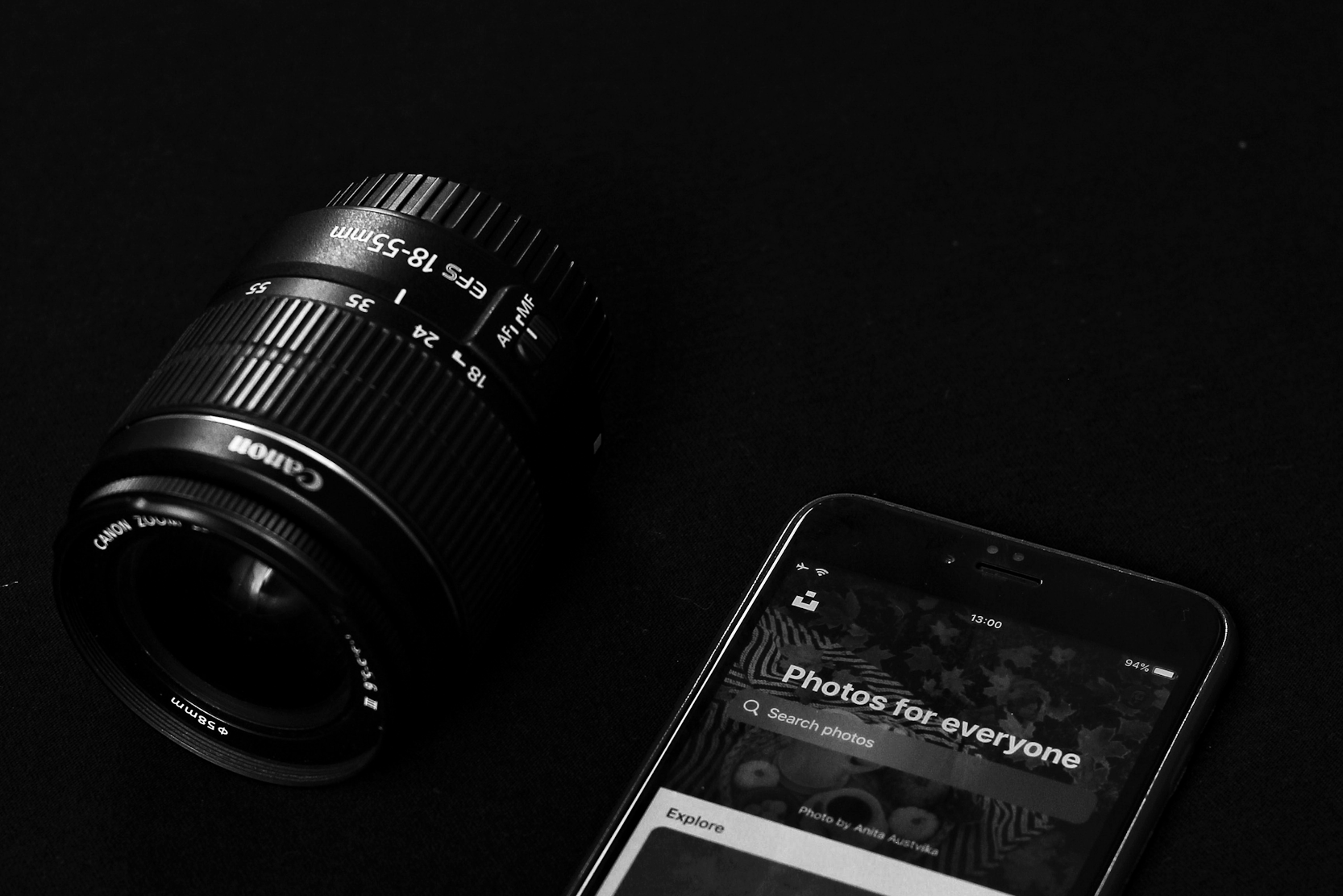 A Canon camera lens and a smartphone displaying a photo app on a black background.