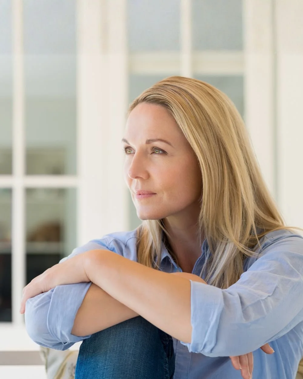 A woman with blonde hair gazing thoughtfully outside a window.