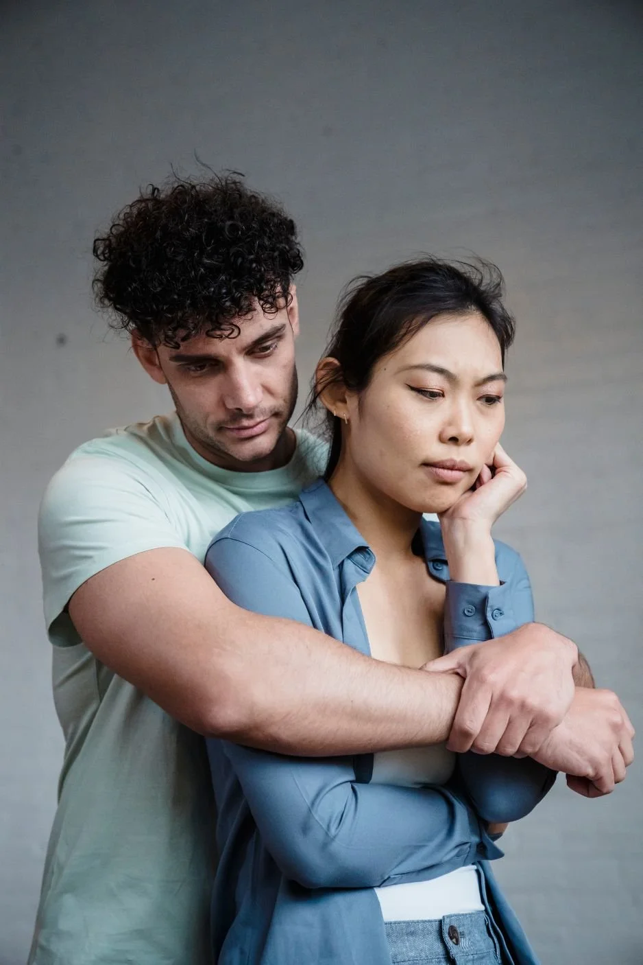 Man wrapping his arms around his partner who seems unhappy