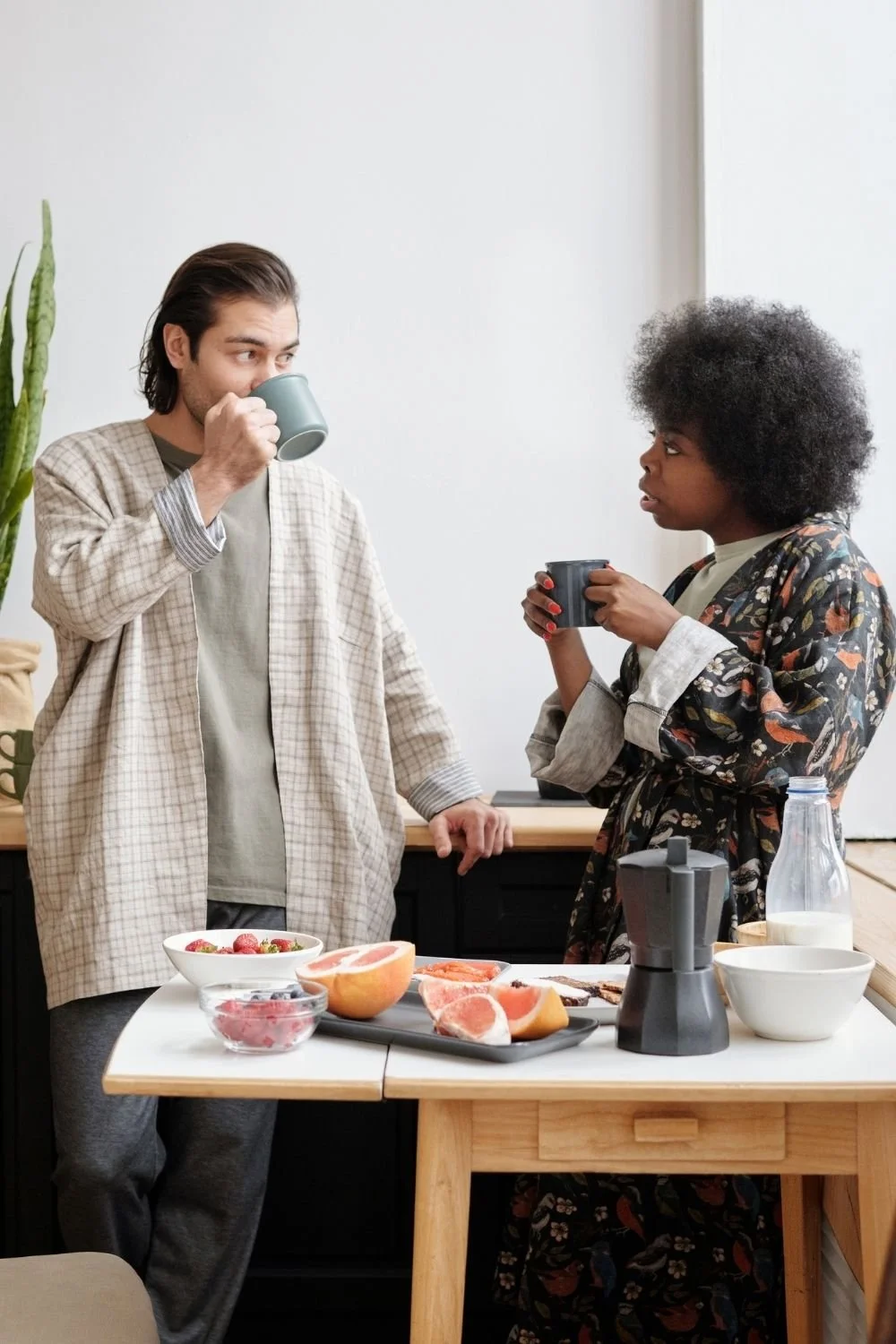 Young biracial couple talking in the kitchen drinking coffee