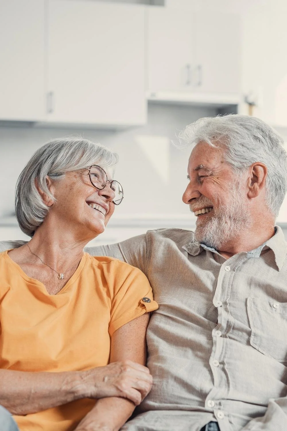 Elderly couple sitting on a couch together smiling at eachother