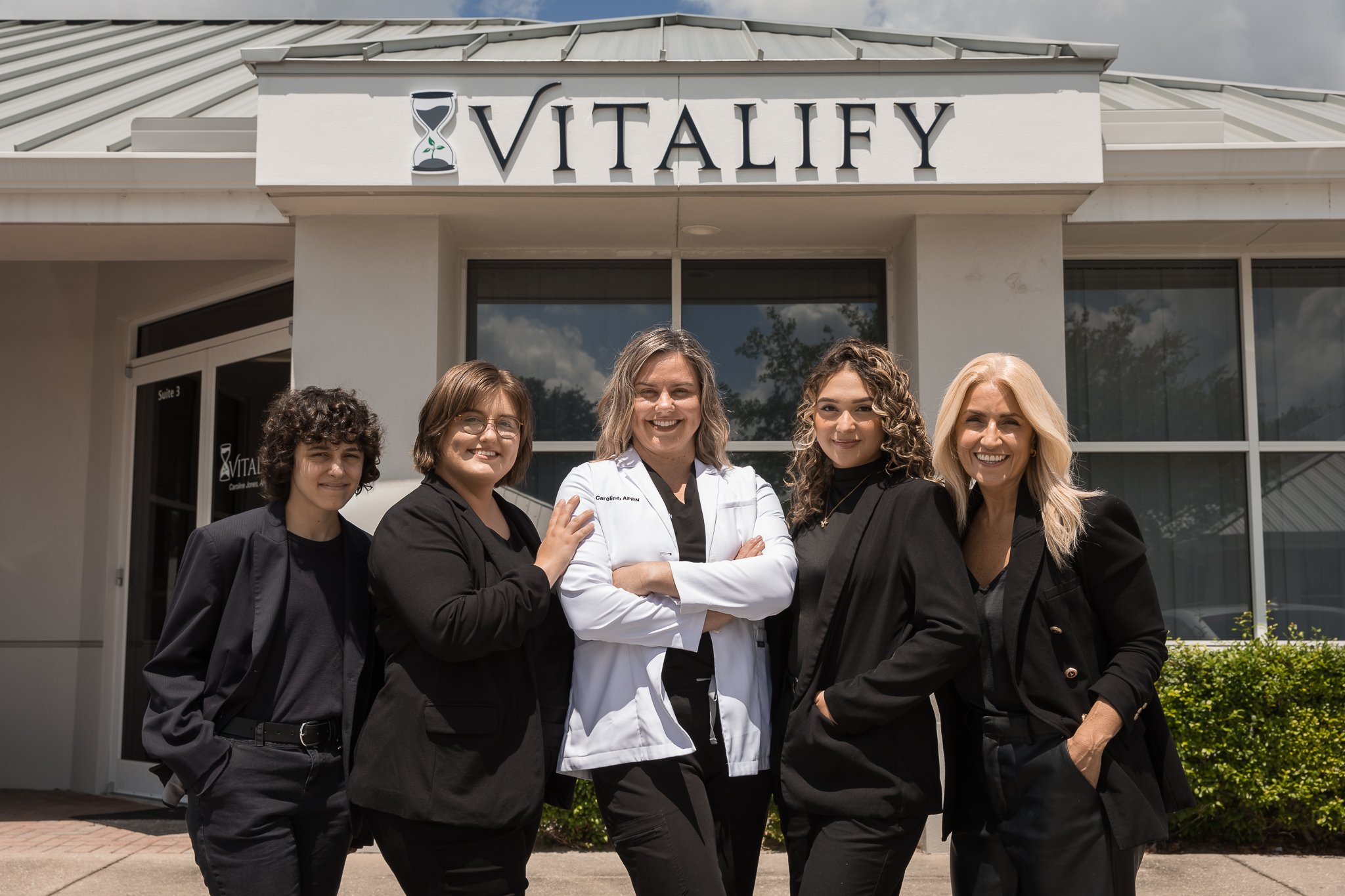 Caroline Jones APRN stands confidently in front of Vitalify's office with her staff