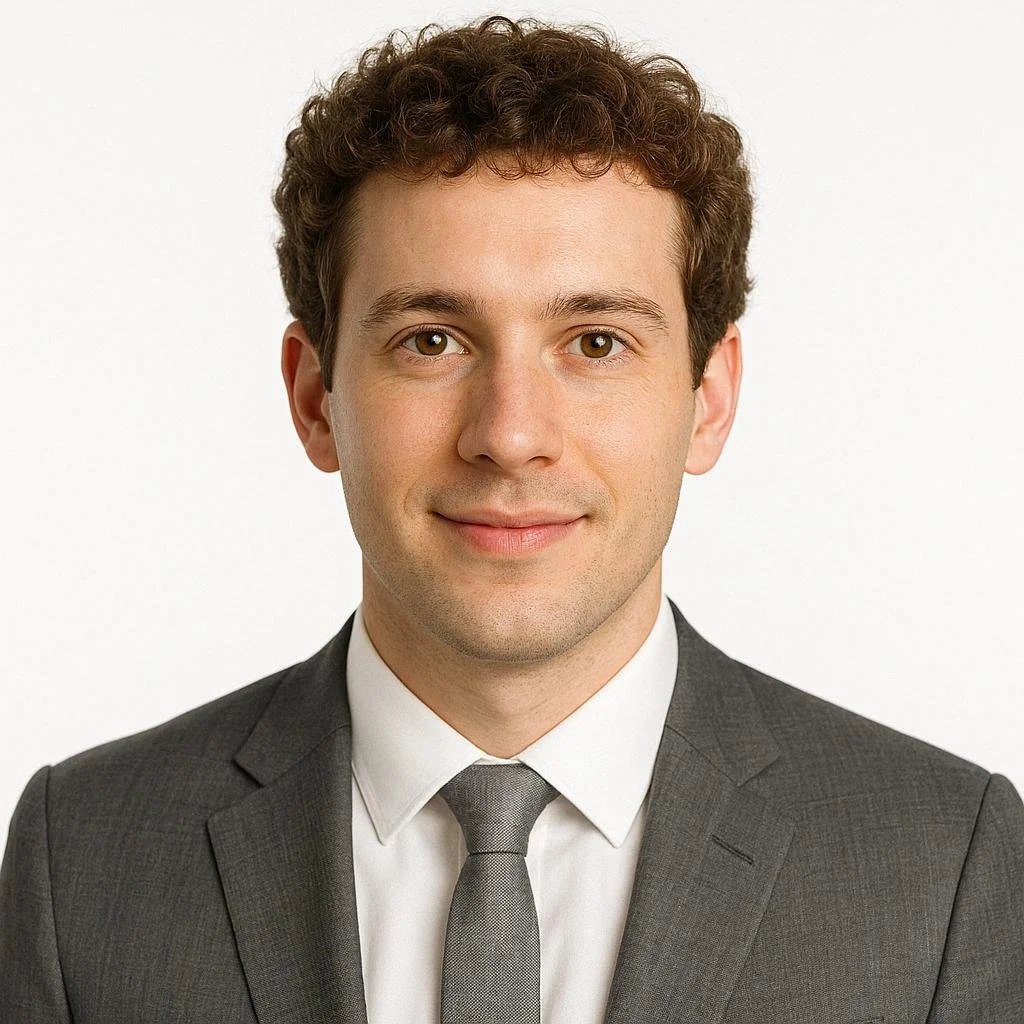 Headshot of a smiling woman with glasses, short curly hair, and wearing a white polka dot shirt on a plain white background.