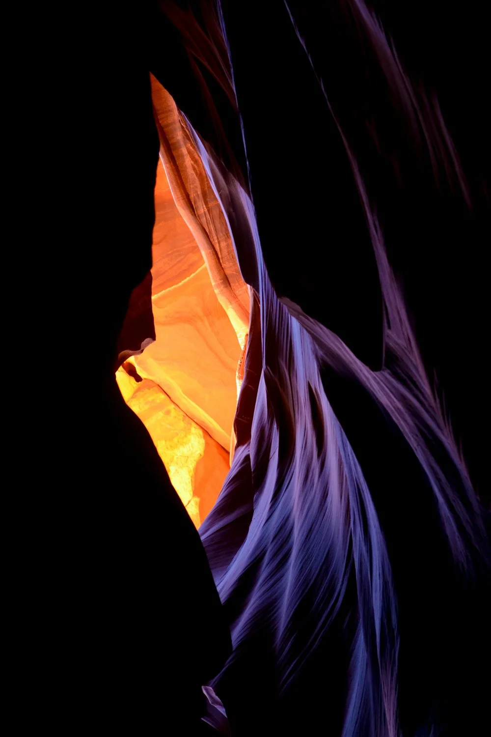 Colorful narrow canyon walls illuminated by sunlight, showcasing orange, purple, and dark hues.