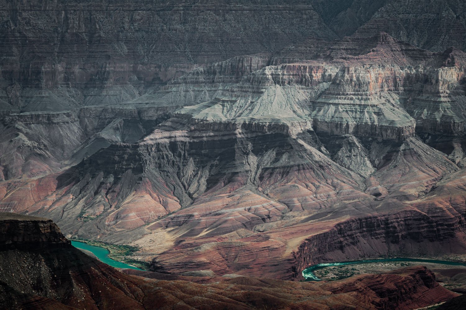 Aerial view of the Grand Canyon with layered rock formations and a winding Colorado River at the bottom.