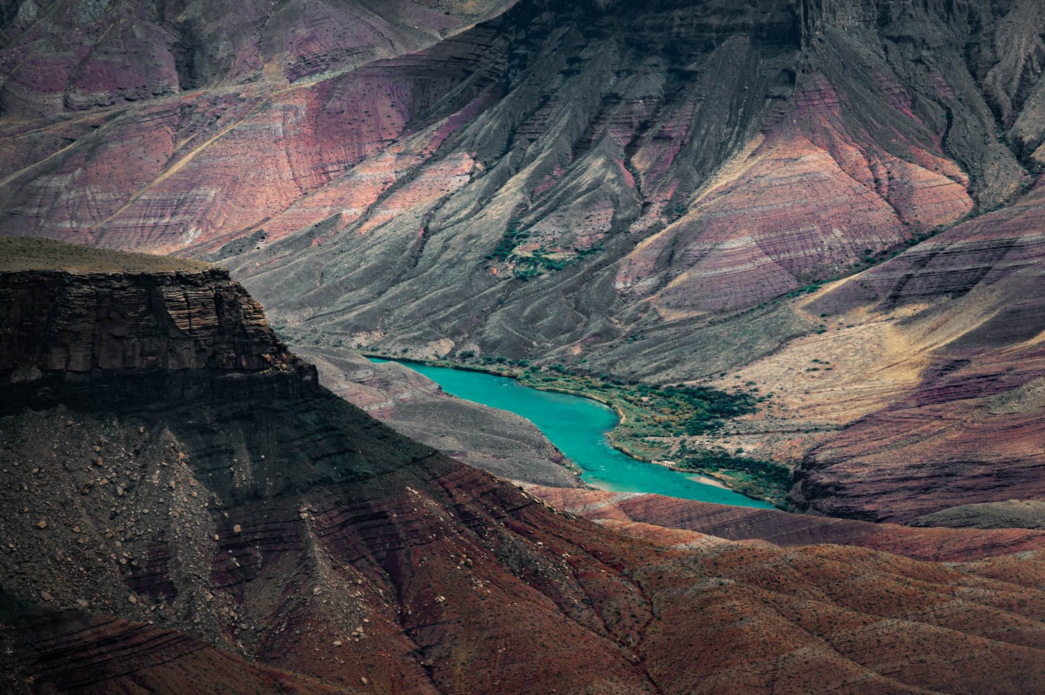 A winding turquoise Colorado River flowing through the colorful Grand Canyon with layered rock formations.