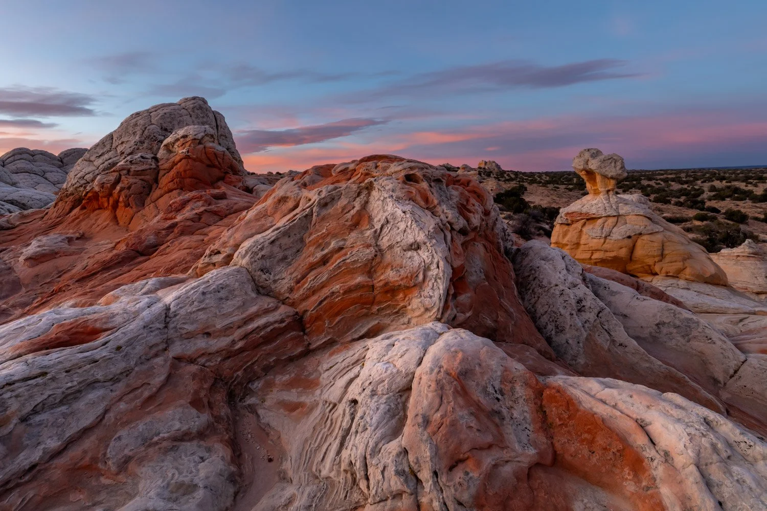 Colorful desert rocks with a hill and sky with pink and purple clouds at sunset in the background.