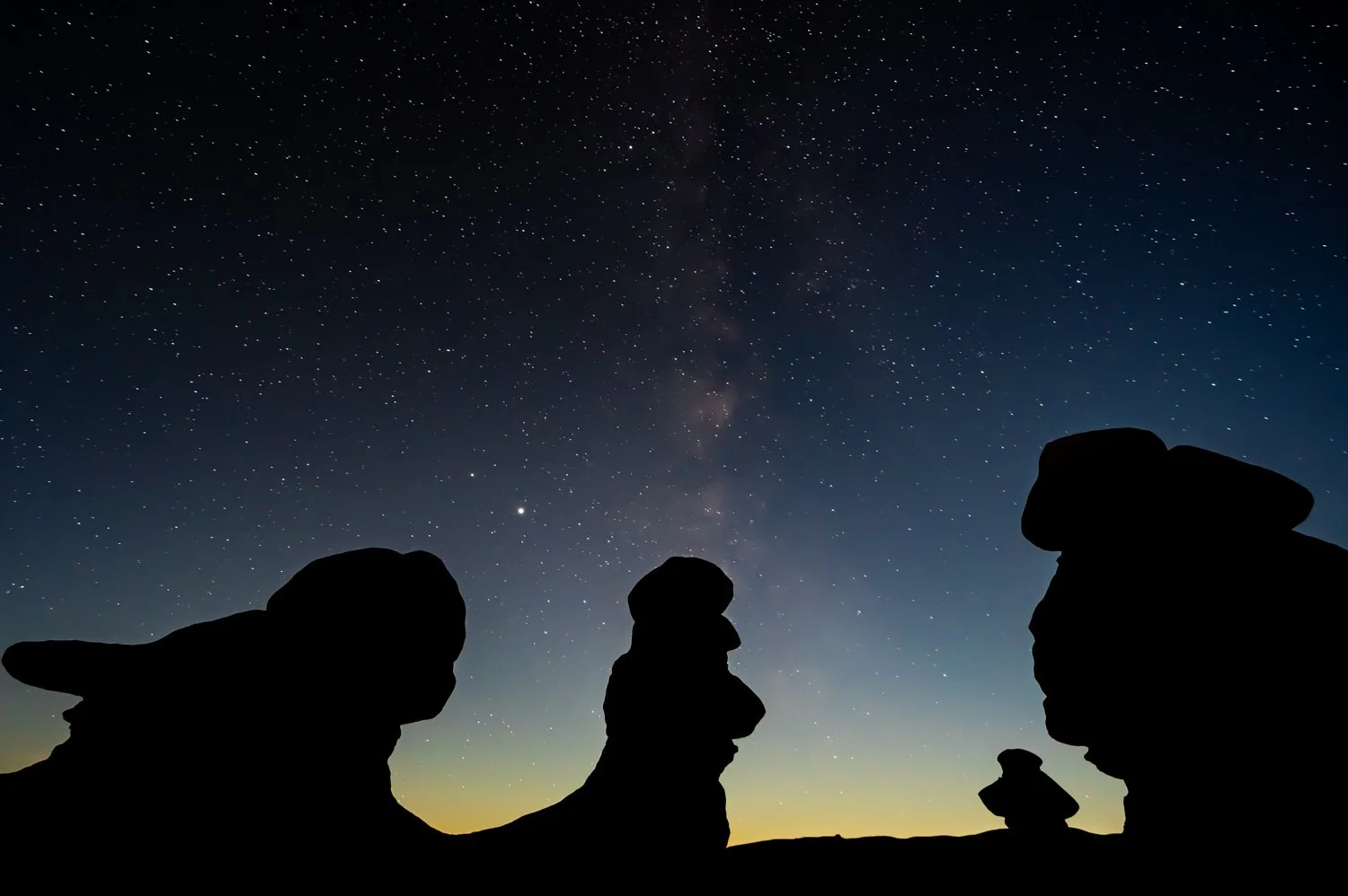 Silhouettes of rock formations under a star-filled night sky with the Milky Way visible.