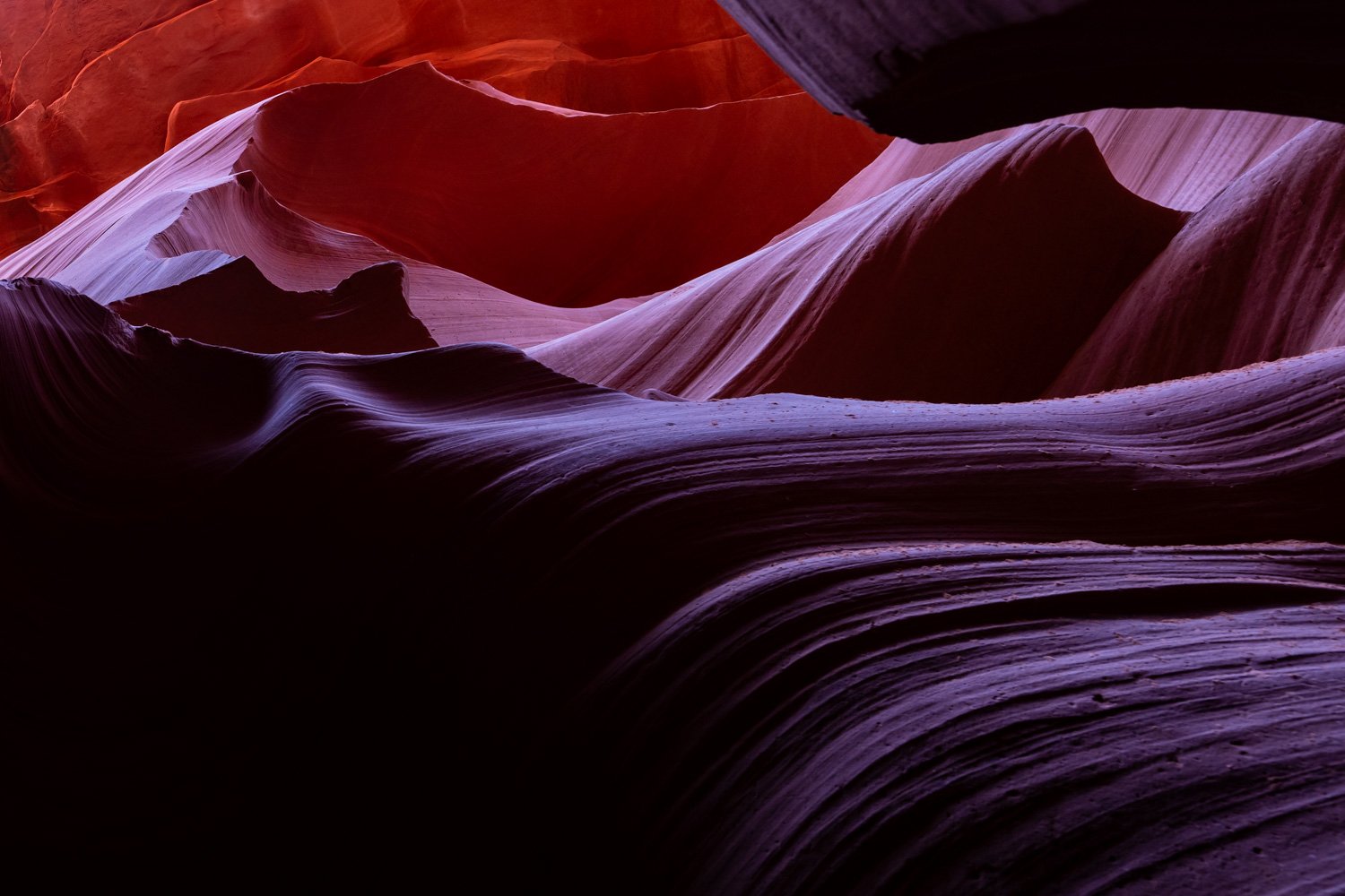 Colorful rock formations with smooth, layered, and curving surfaces in shades of purple, pink, and red.