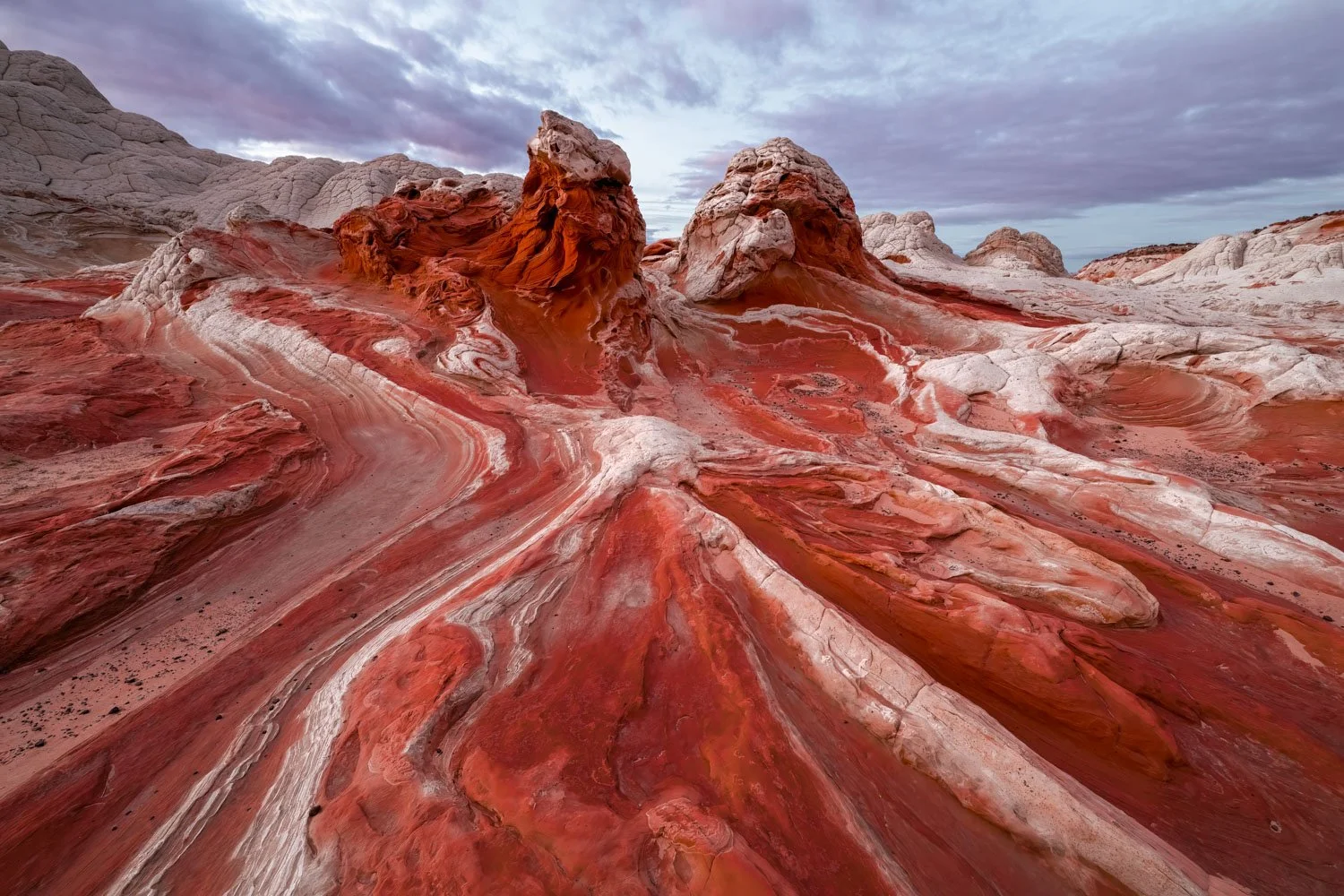 Colorful rock formations with swirling red, pink, and white layers in a desert landscape under a cloudy sky.