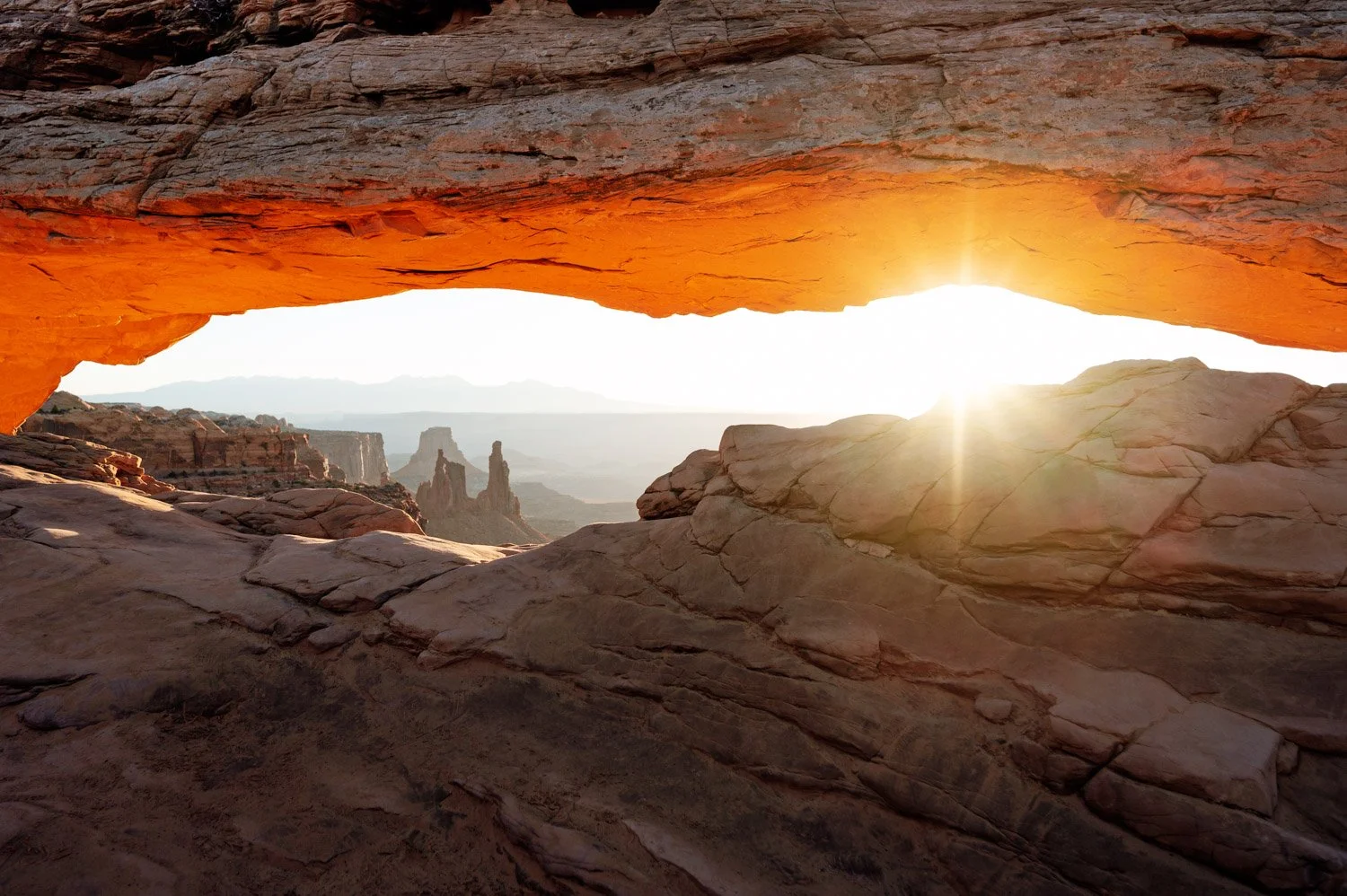 Sunrise view through a natural rock arch in a desert landscape with distant canyon formations
