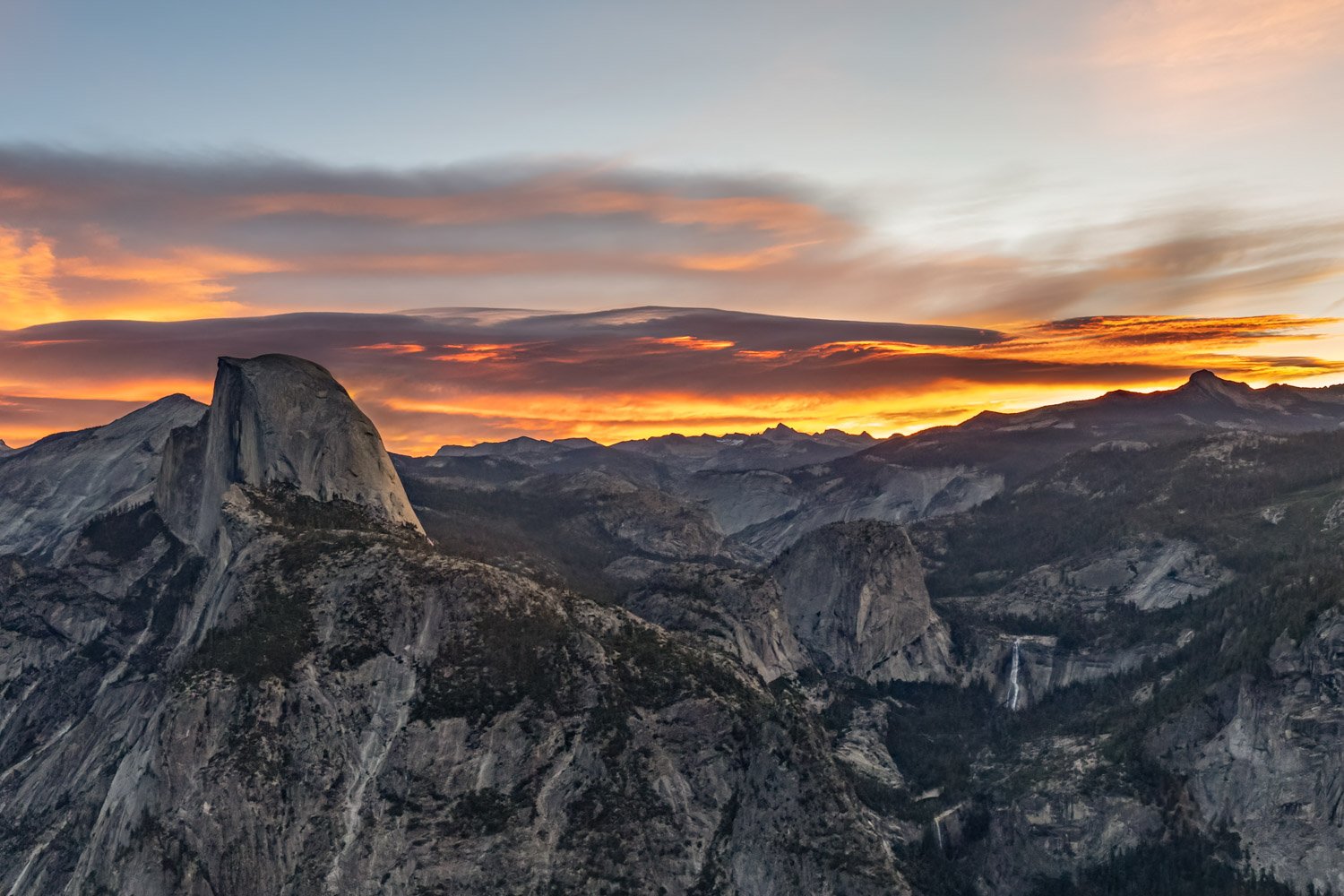 Sunrise over a mountainous landscape with prominent granite cliffs and a waterfall in the distance