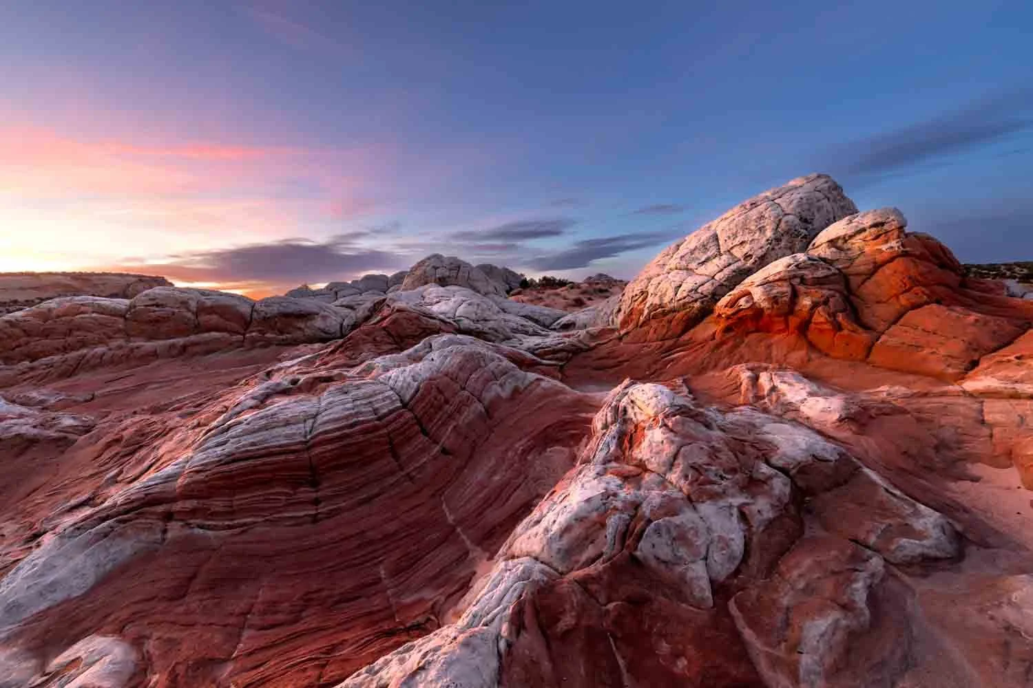Colorful rock formations with layered patterns in a desert landscape under a partly cloudy sky at sunrise.