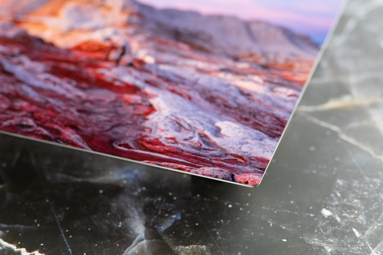 Close-up of a glossy printed photograph of a rocky landscape with reddish hues, resting on a dark, textured surface.
