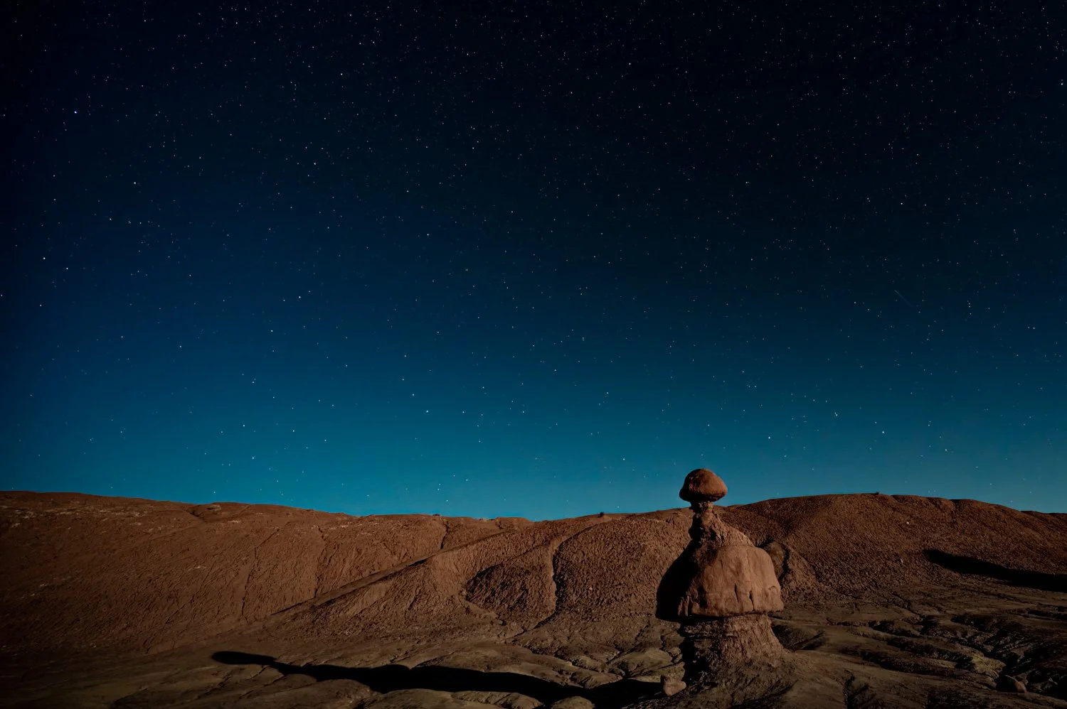 Desert landscape at night with stacked rocks in the foreground and a starry sky above.