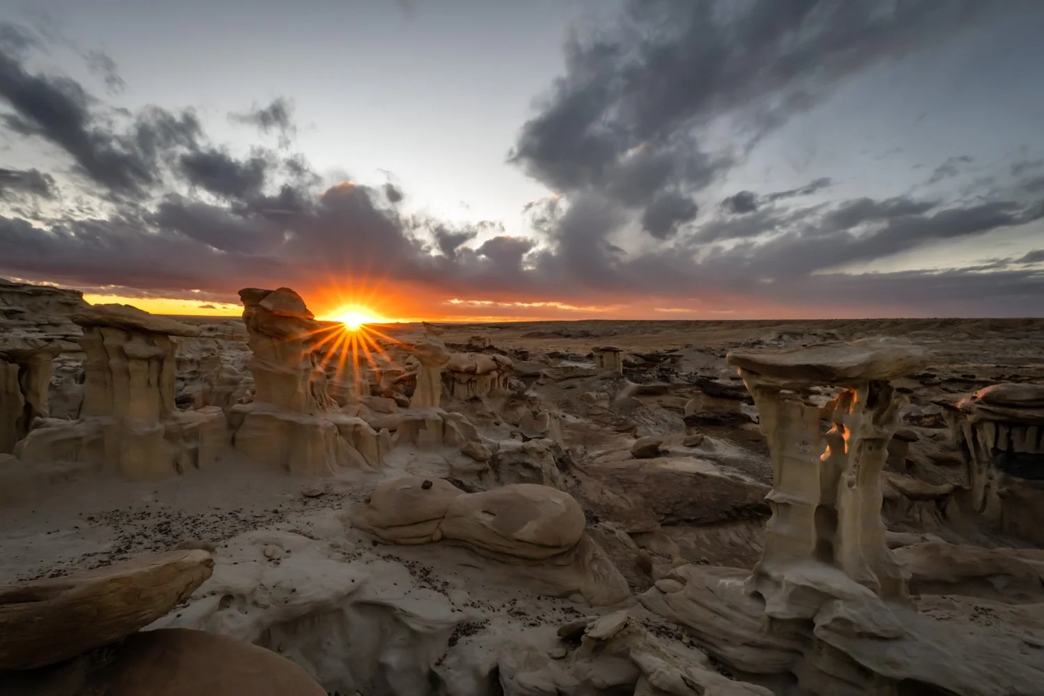 Sandstone hoodoos in a desert at sunset with dramatic clouds in the sky.