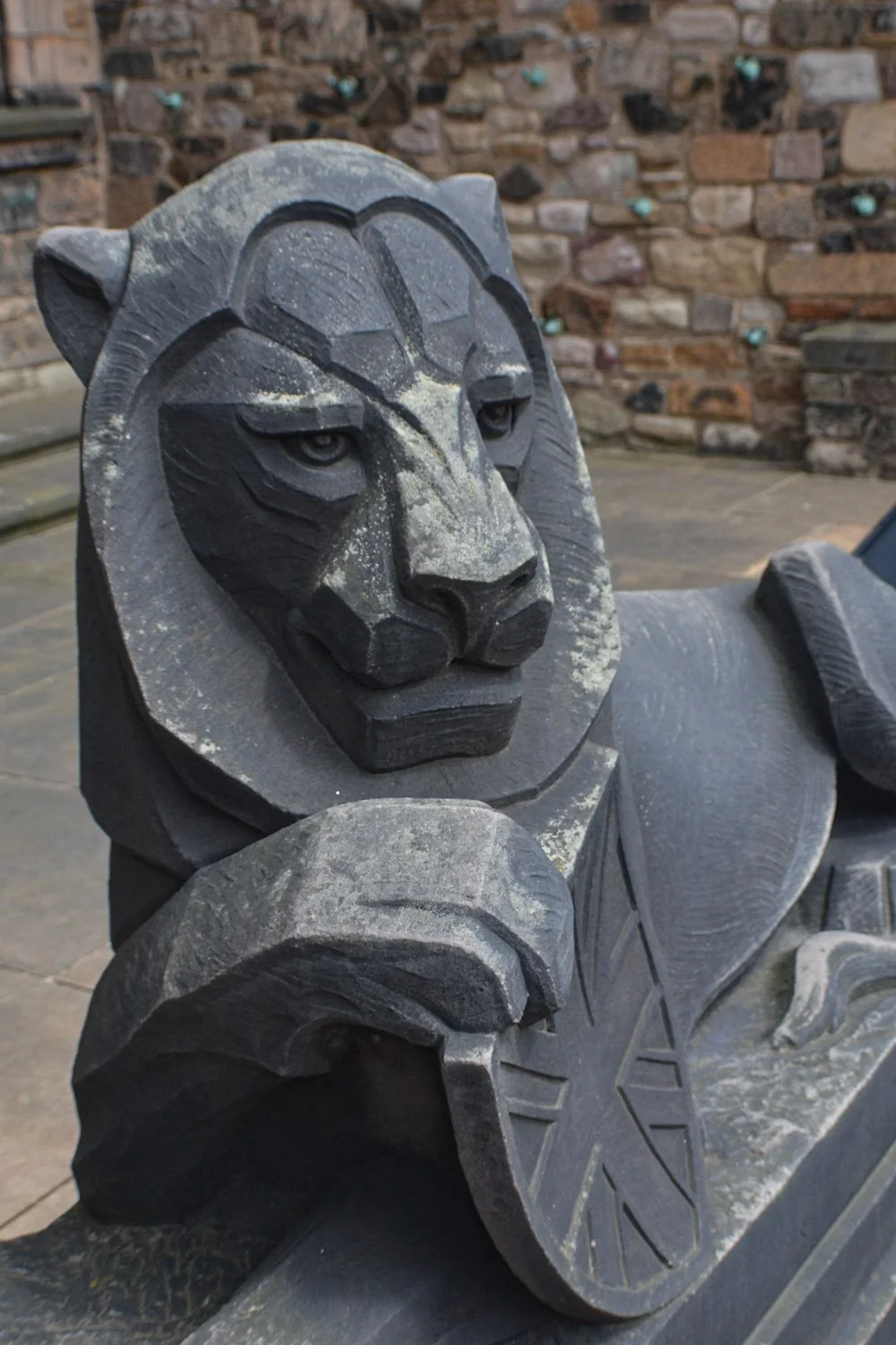 A close-up view of a carved stone statue of a lion lying down with a detailed face and a star engraved on its front paw, set against a background of a stone wall.