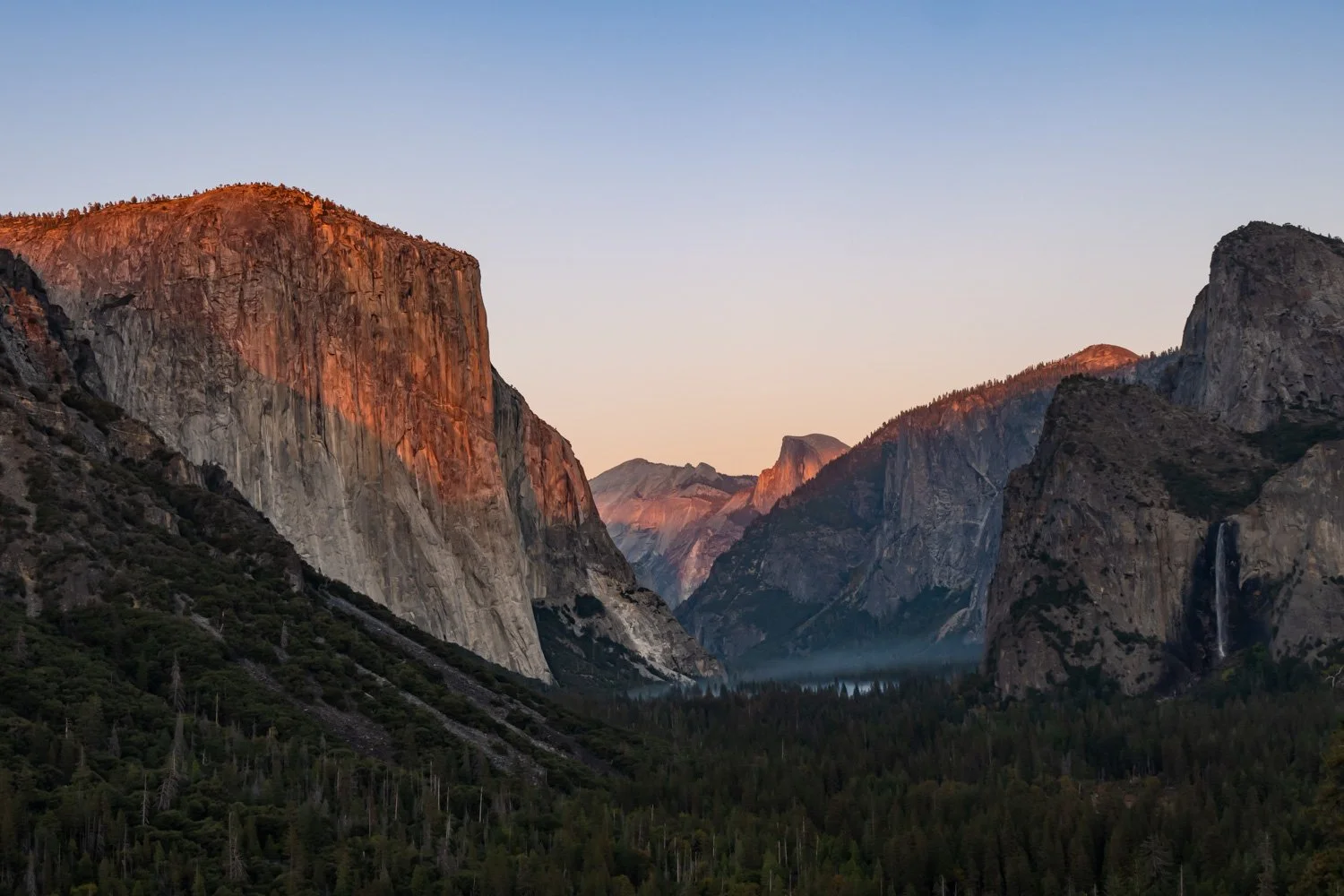 View of Yosemite Valley with tall granite cliffs and forested valley floor during sunset
