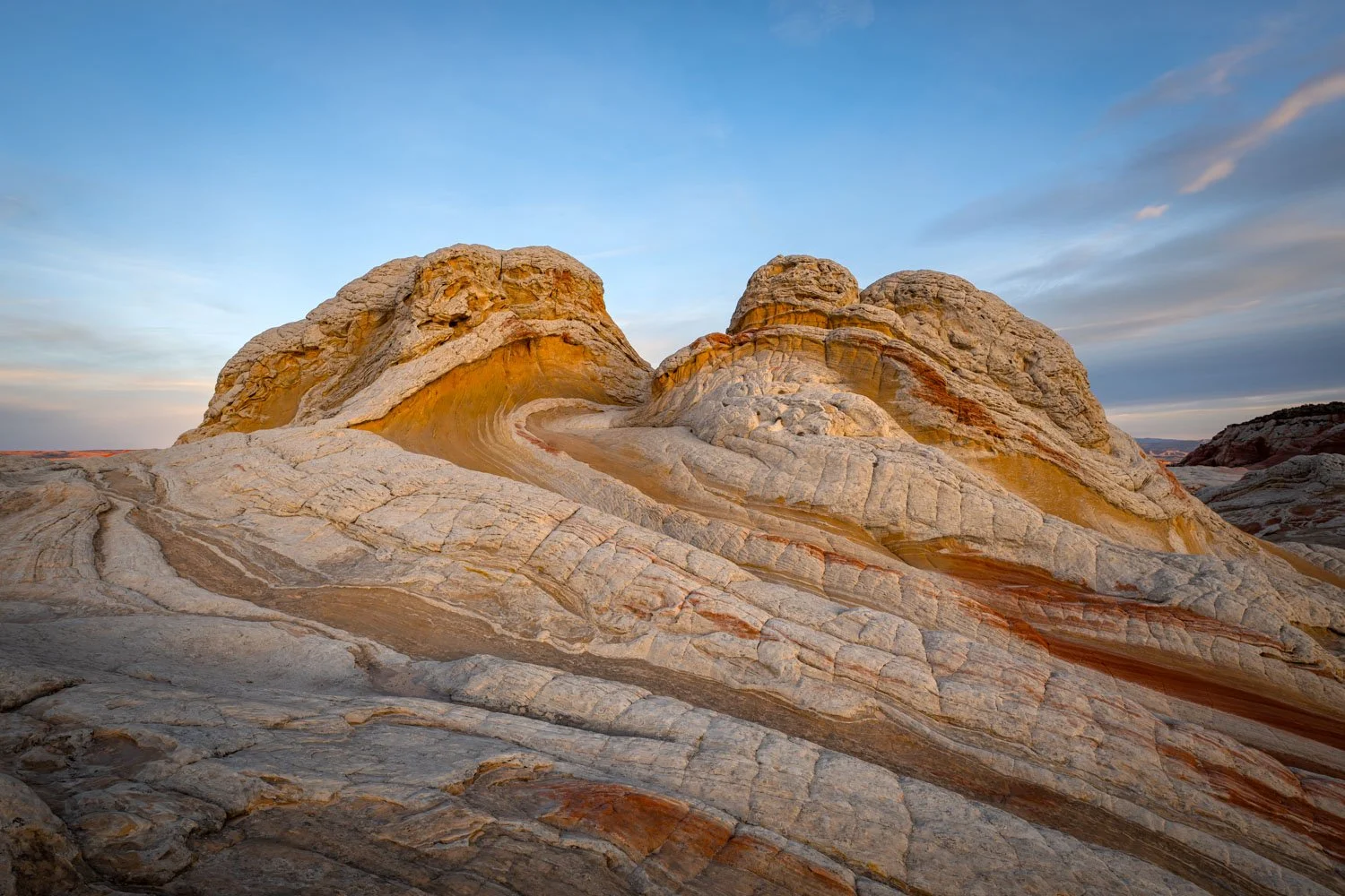 Colorful layered rock formations on a desert landscape under a partly cloudy sky at sunset.