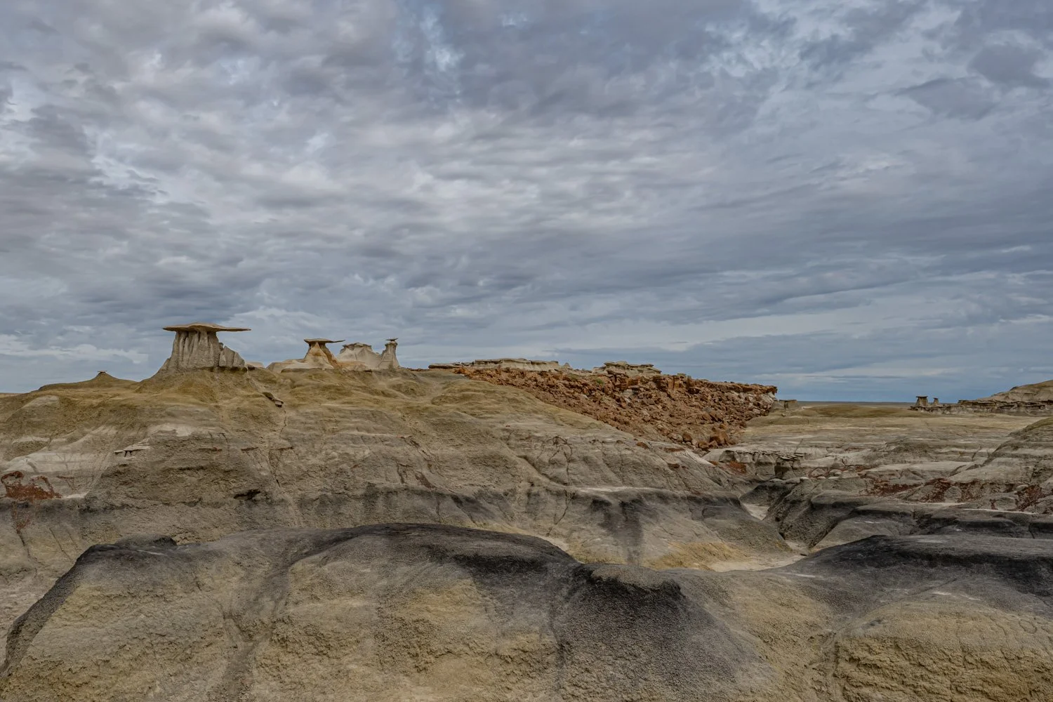 A desert landscape with unique hoodoo rock formations under a cloudy sky, featuring layered sedimentary rocks and eroded formations.