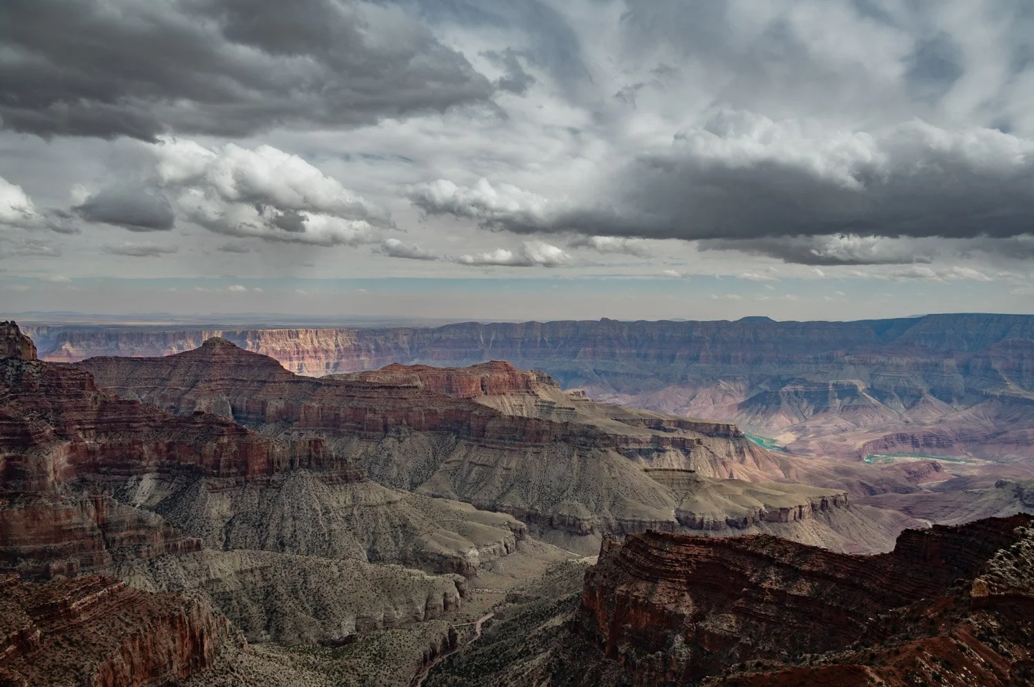 View of the Grand Canyon with layered rock formations and a cloudy sky overhead.