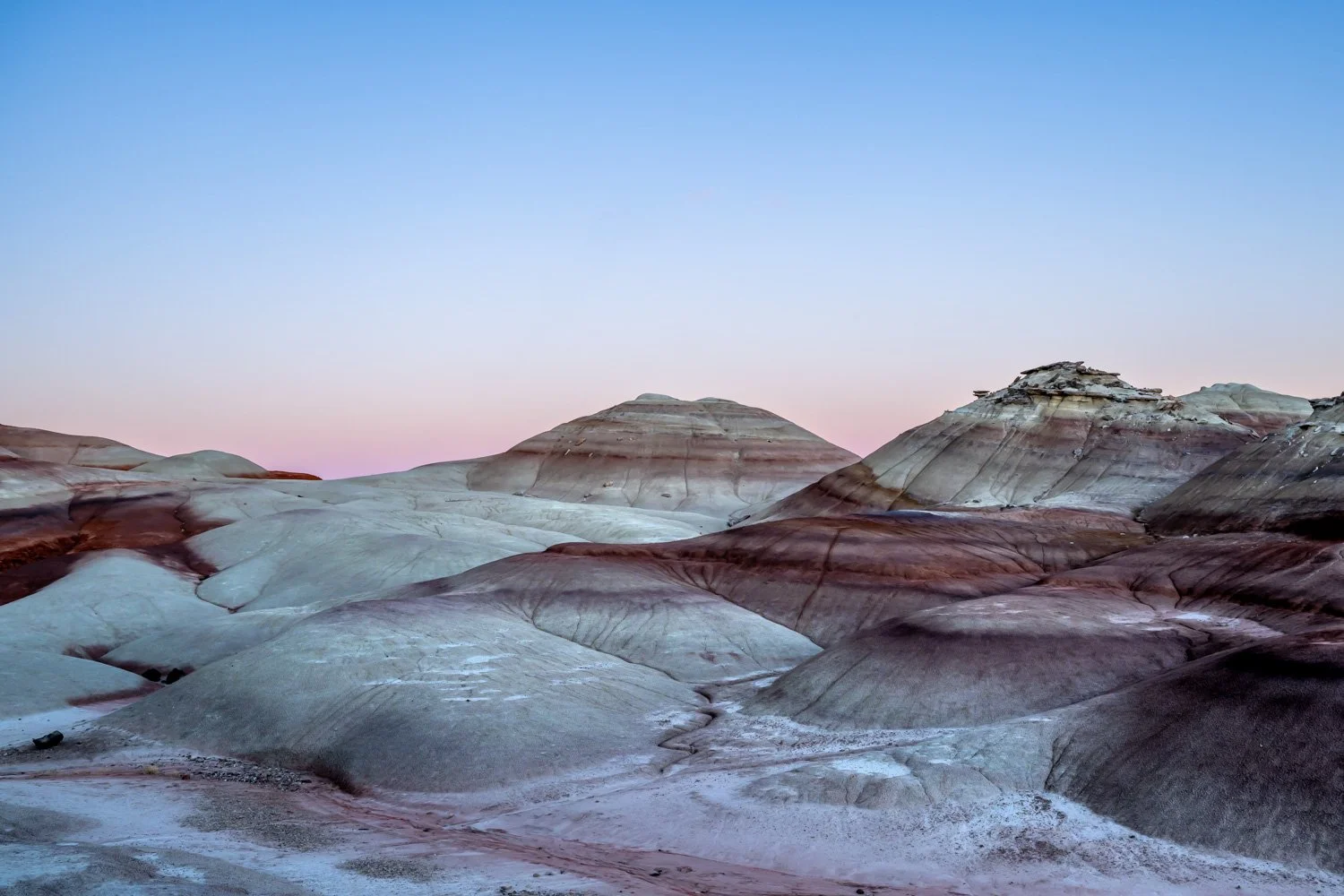 Colorful layered rock formations in a desert landscape under a clear blue sky during sunset.