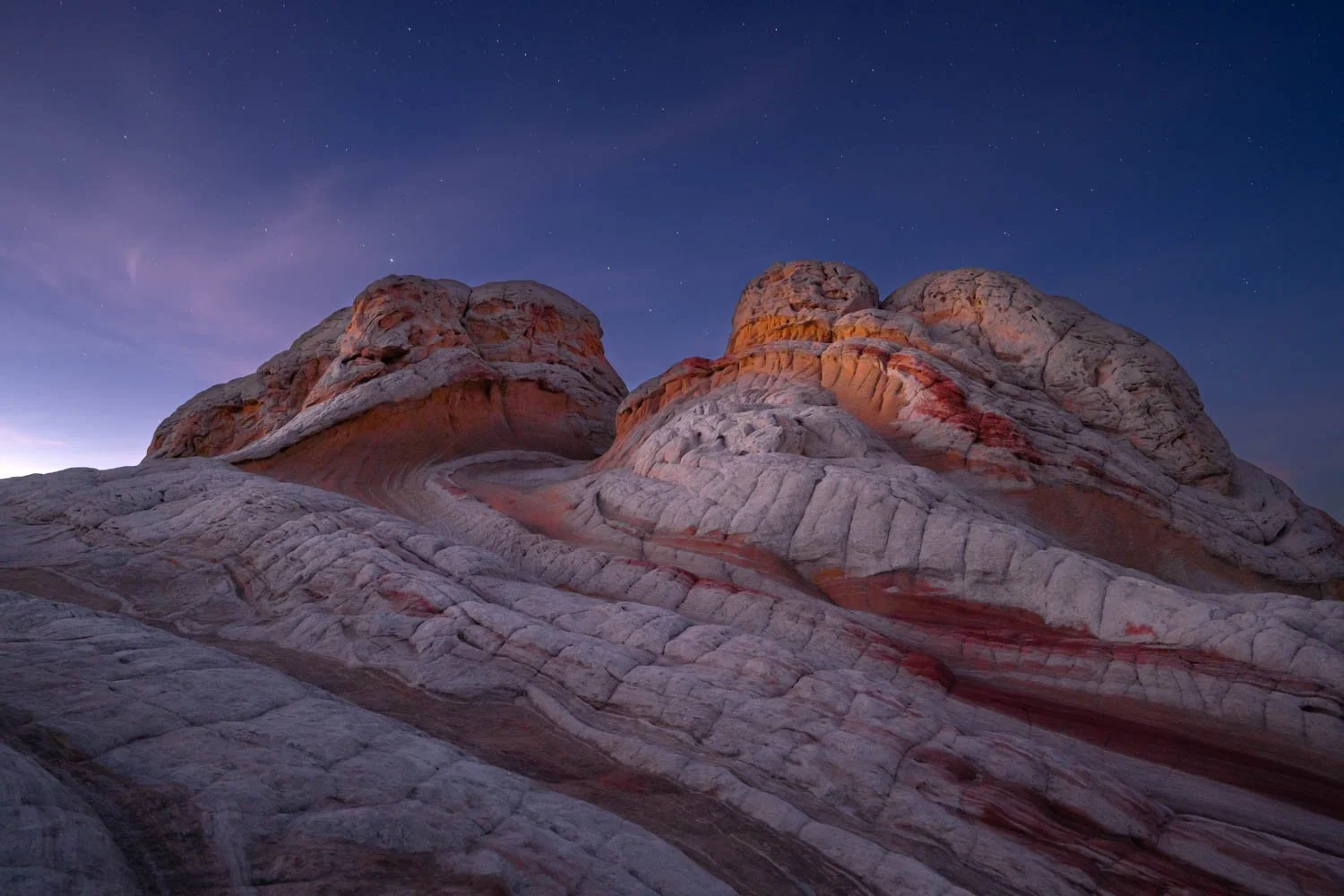 View of colorful striped rock formations at dusk with a starry sky in the background.