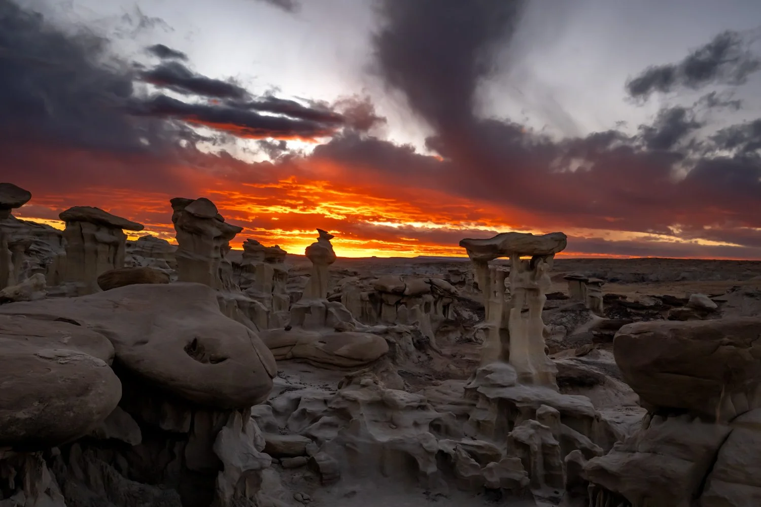 A desert landscape at sunset with rock formations and dramatic clouds in the sky.