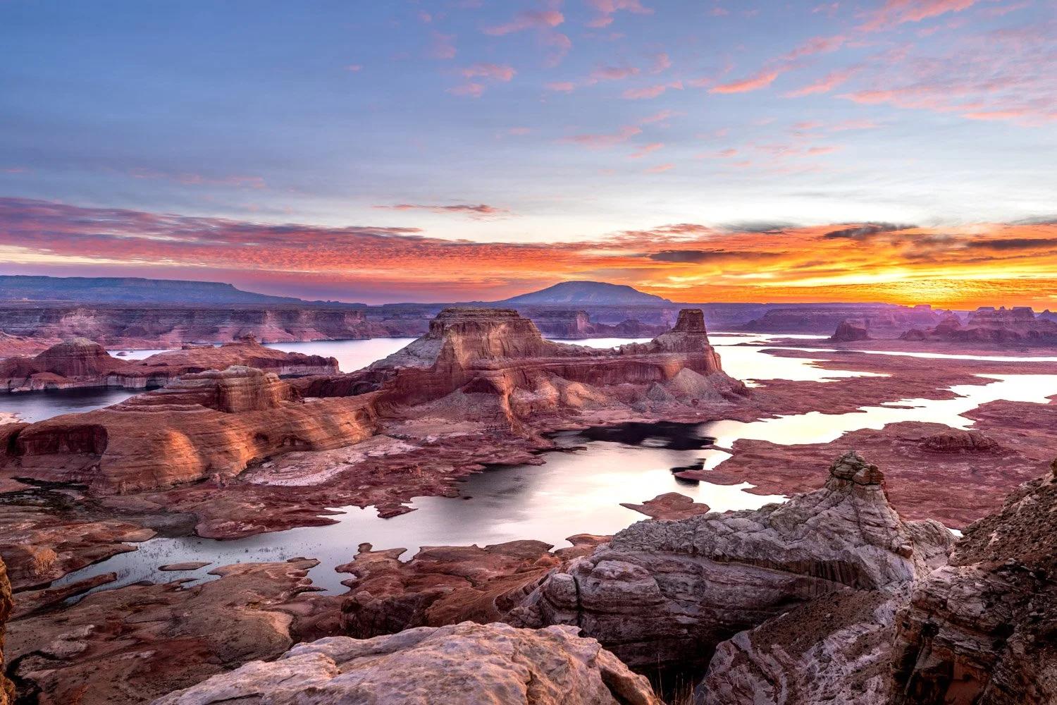 Sunrise over the Lake Powell at Alstrom Point with colorful sky, rocky formations, and water reflecting the sky's colors.