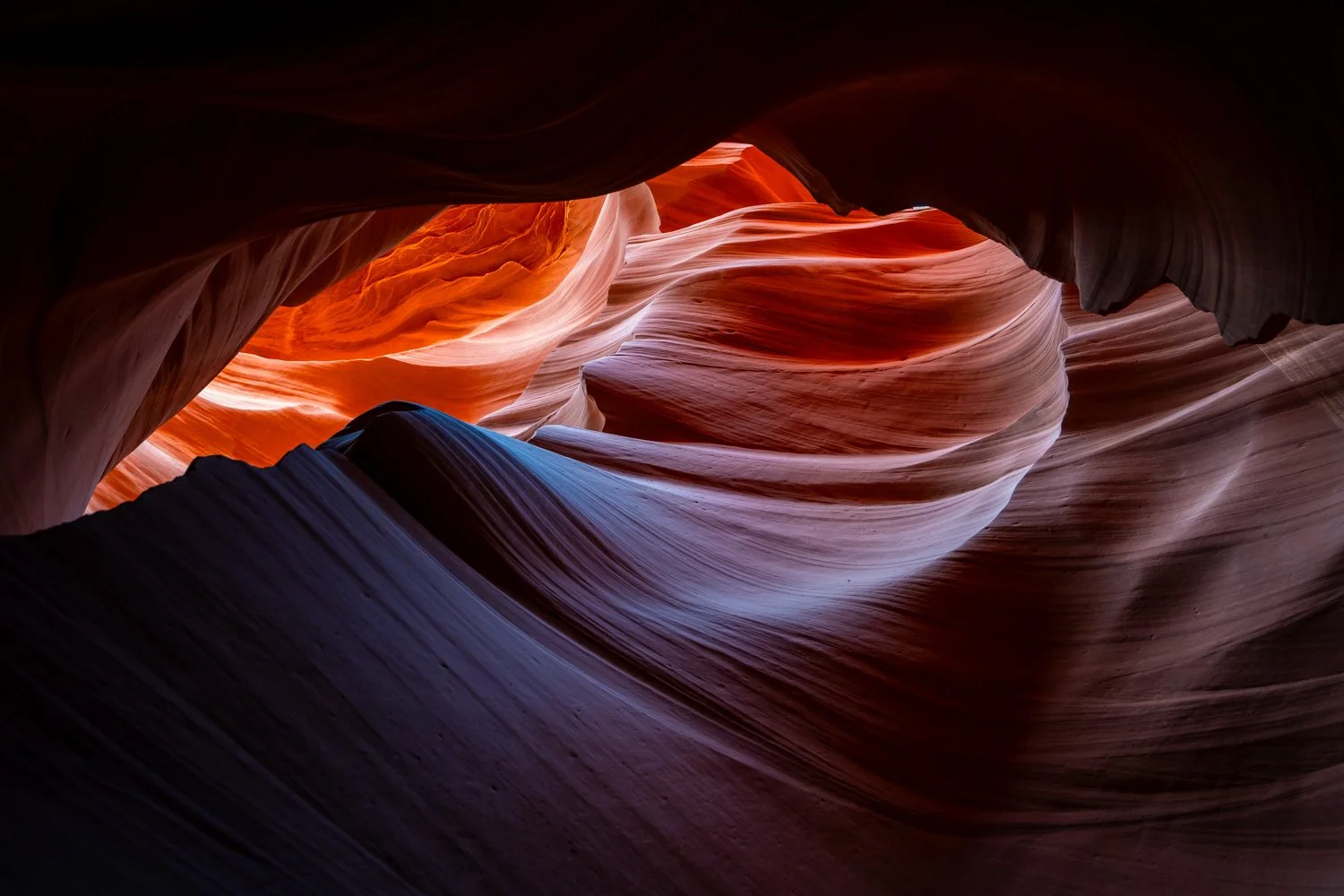 An inspiring view of a colorful slot canyon with curving sandstone walls in shades of orange, red, and purple, illuminated by soft natural light.