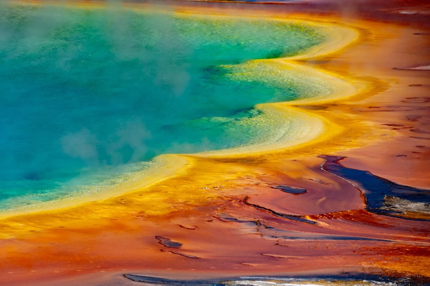 Colorful geothermal hot spring with vibrant turquoise water, yellow mineral deposits along the edge, and reddish-brown soil surrounding it.