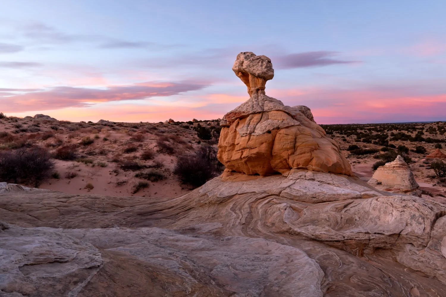 Unique rock formation in a desert landscape during sunset, with pink and purple clouds in the sky.