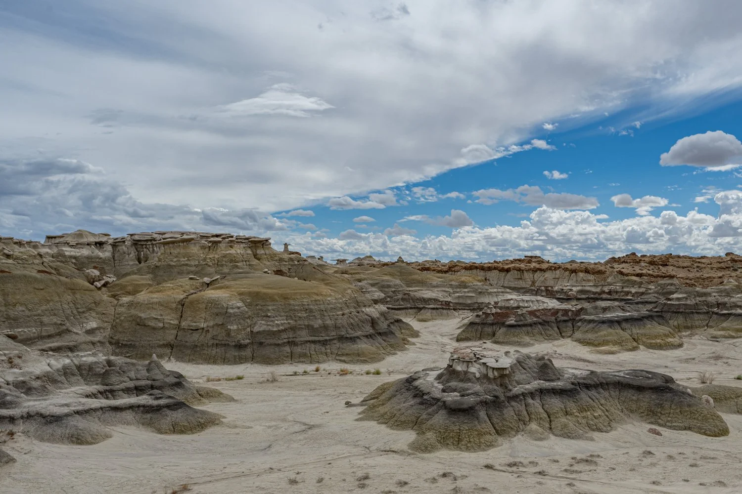 A barren desert landscape with layered rock formations under a partly cloudy sky.