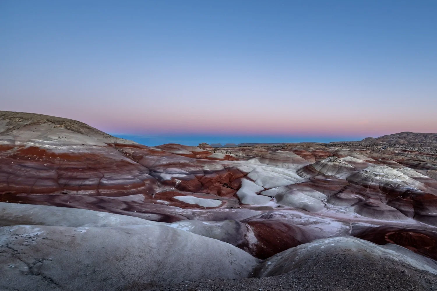 Colorful, layered rock formations in a desert landscape at dusk with a gradient sky.