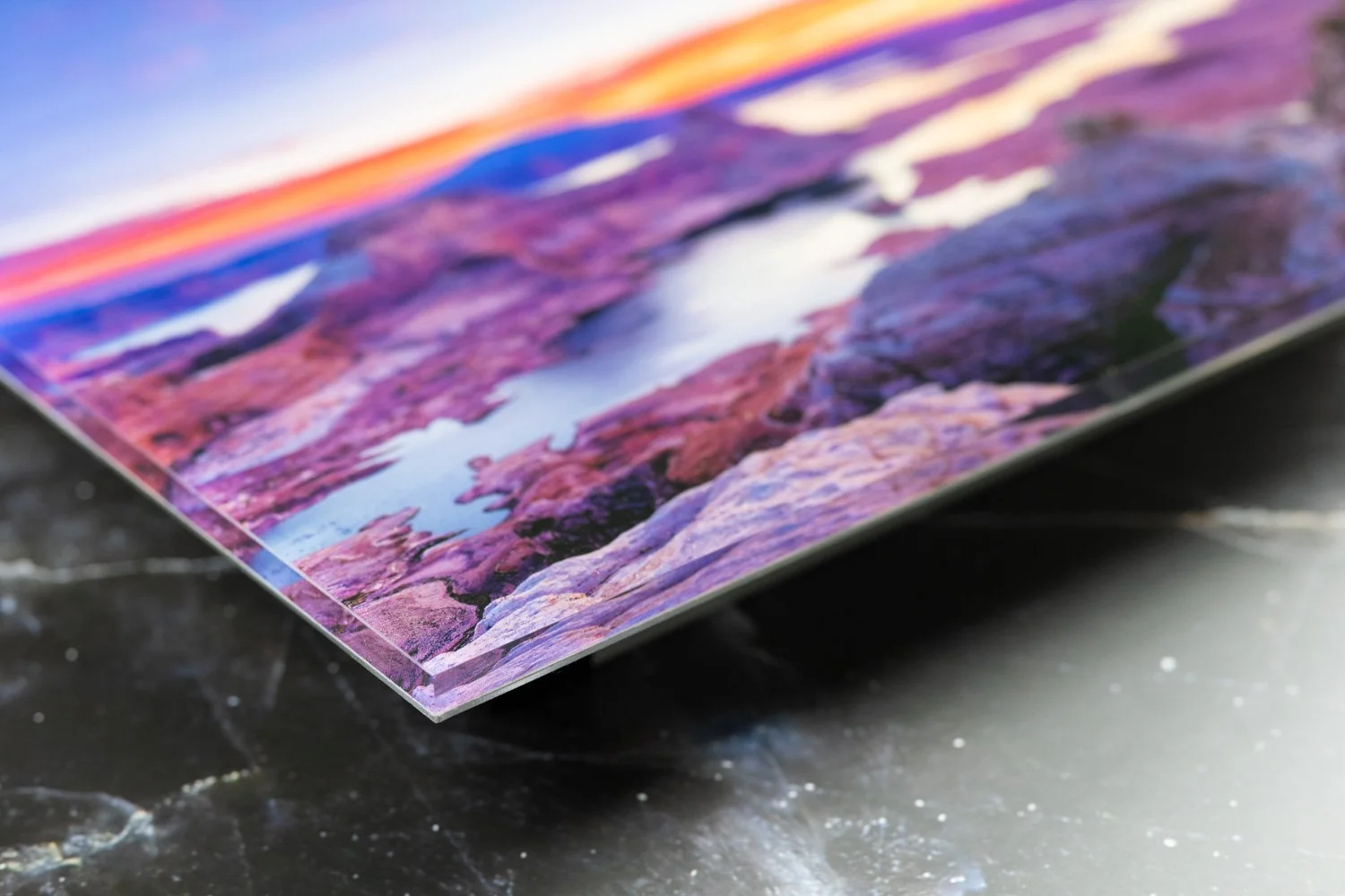 Close-up of a glossy photo print of a colorful landscape with mountains and a lake, resting on a dark surface.