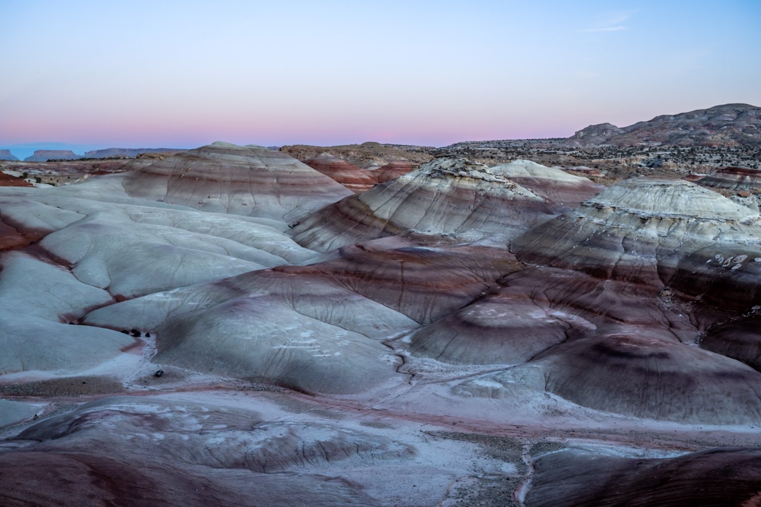Colorful layered rock formations in a desert landscape at dusk with a pastel pink and blue sky.