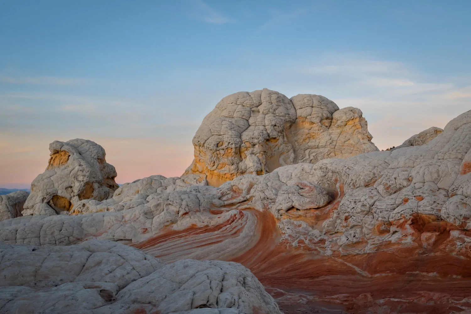 A landscape of white and orange layered rocks with a blue sky and sparse clouds in the background.