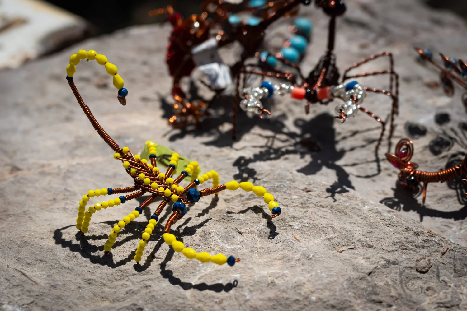 Colorful beaded sculptures of insects, including a yellow and brown spider and a multicolored spider, on a rocky surface.