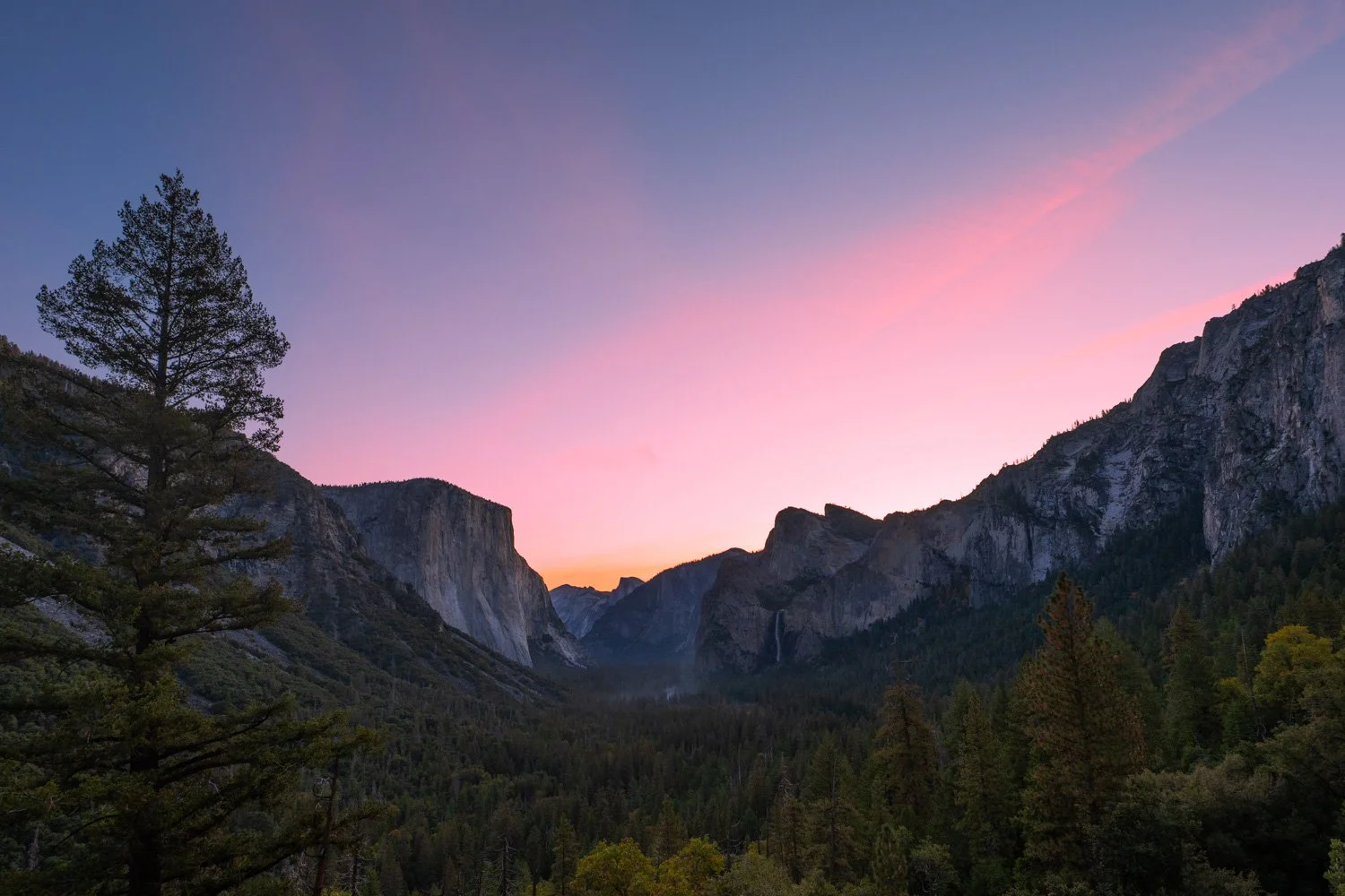 Sunset over a mountainous valley with trees in the foreground and cliffs on either side