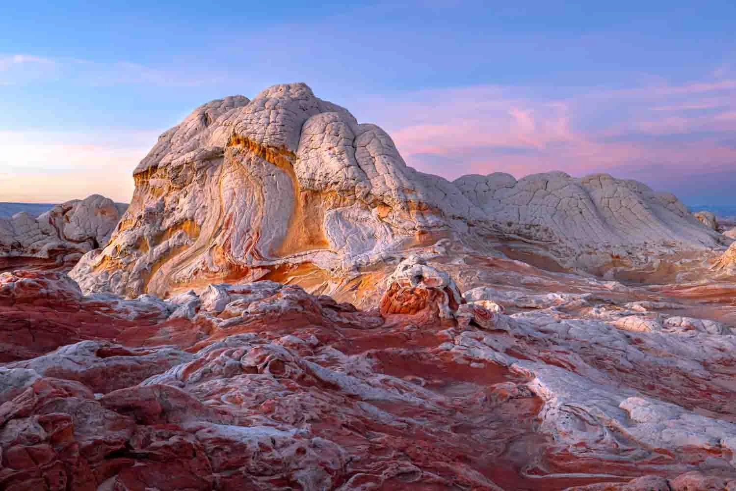 Colorful rock formations with swirling patterns in a desert landscape at sunset.