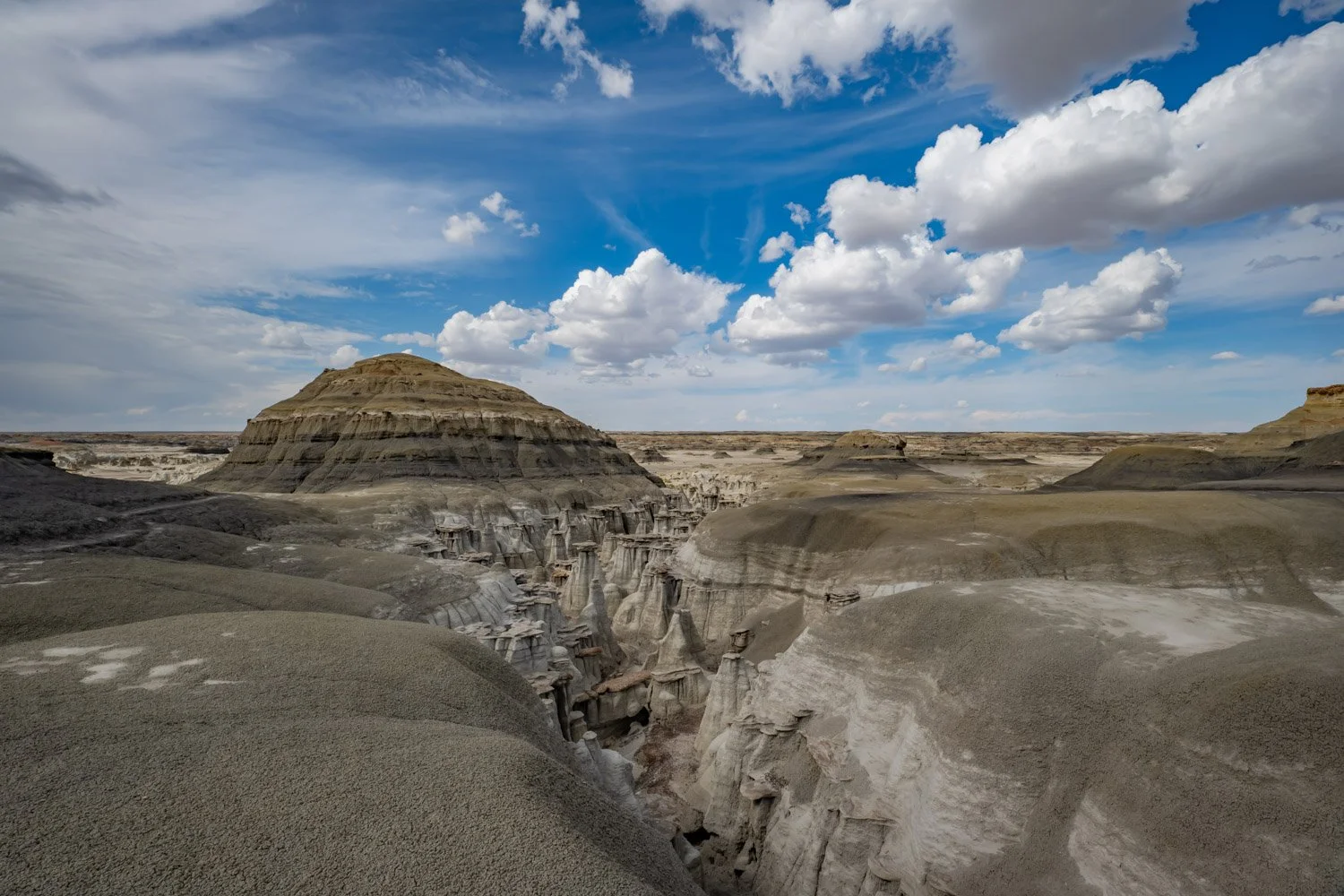 A rugged canyon landscape with rock formations and layered cliffs under a partly cloudy blue sky.