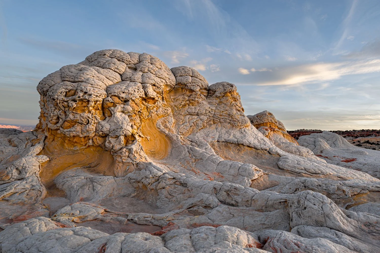 Sunlit rocky desert landscape with layered, weathered stone formations under a partly cloudy sky.