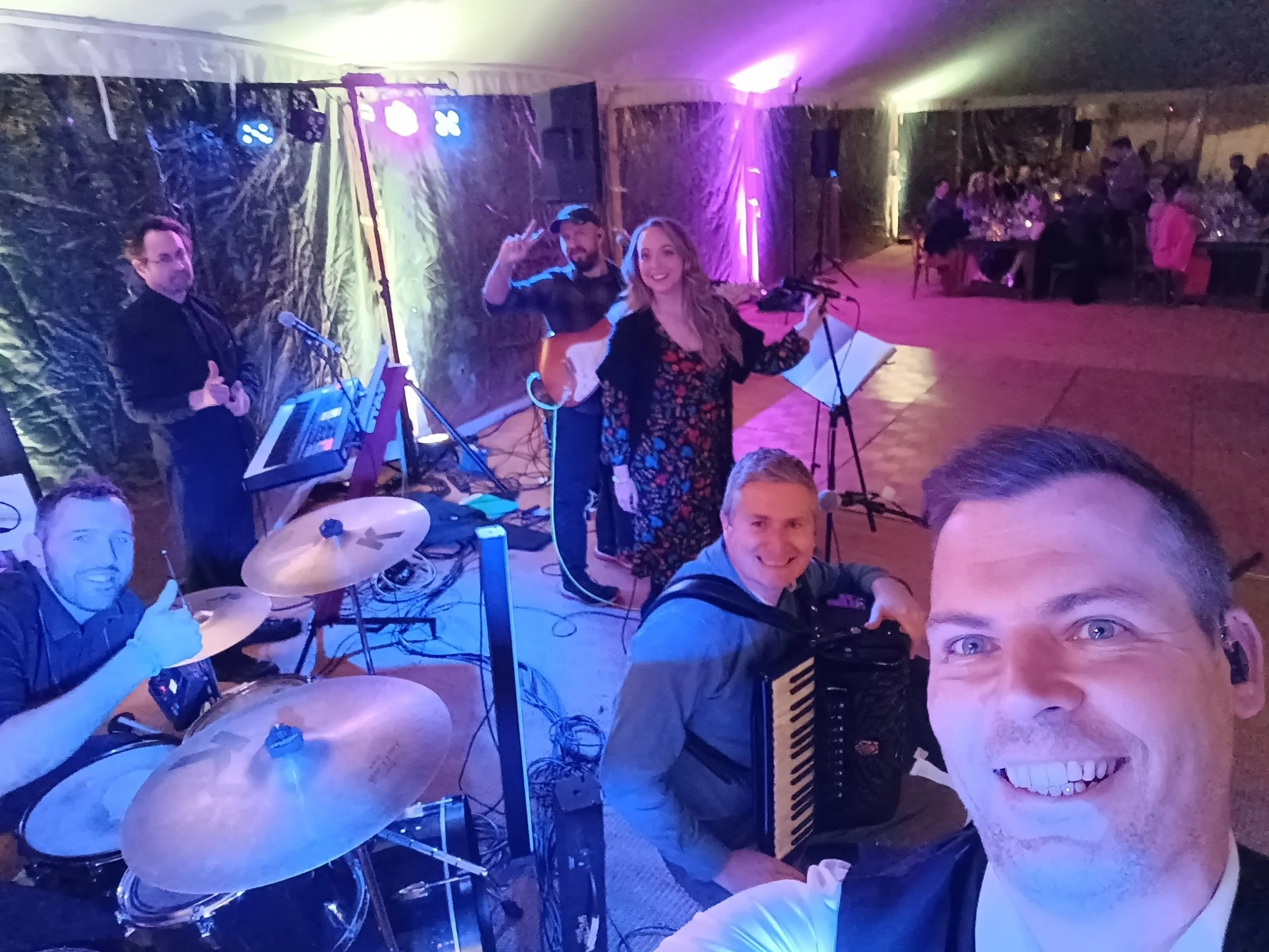 Group of musicians performing at a decorated indoor event with guests seated at tables in the background. Croy, wedding, live band, marquee tent, highland stretch tents, KBE Events