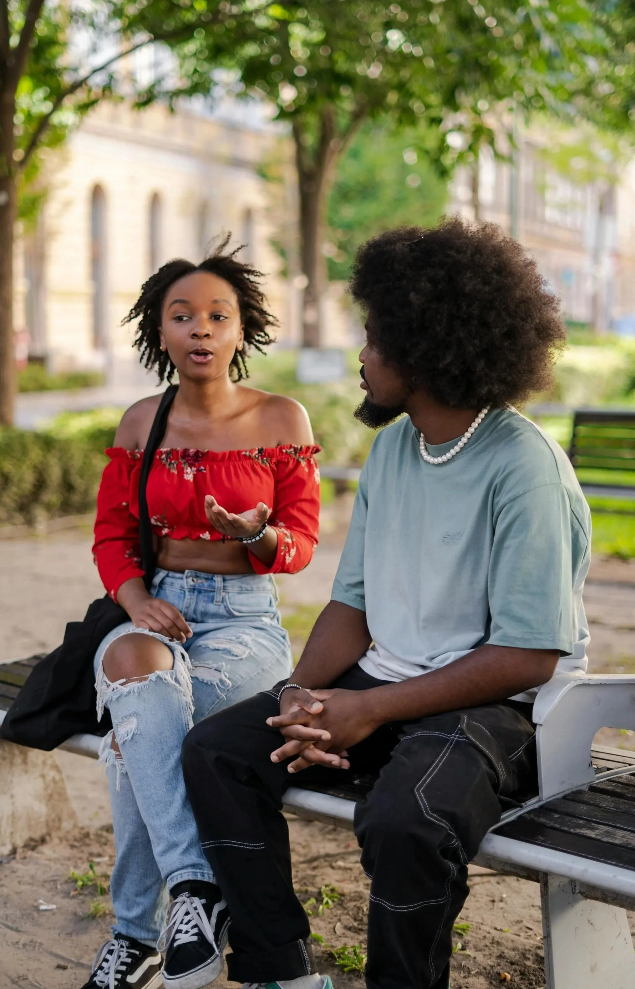 A young man and woman of color sitting on a bench with trees behind them having a conversation about marriage counseling in Worcester.