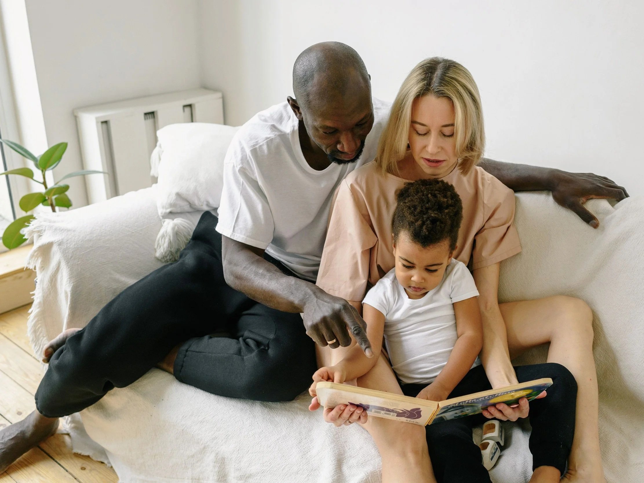 Interracial couple reading with their toddler son on the couch at Couples Therapy Massachusetts.