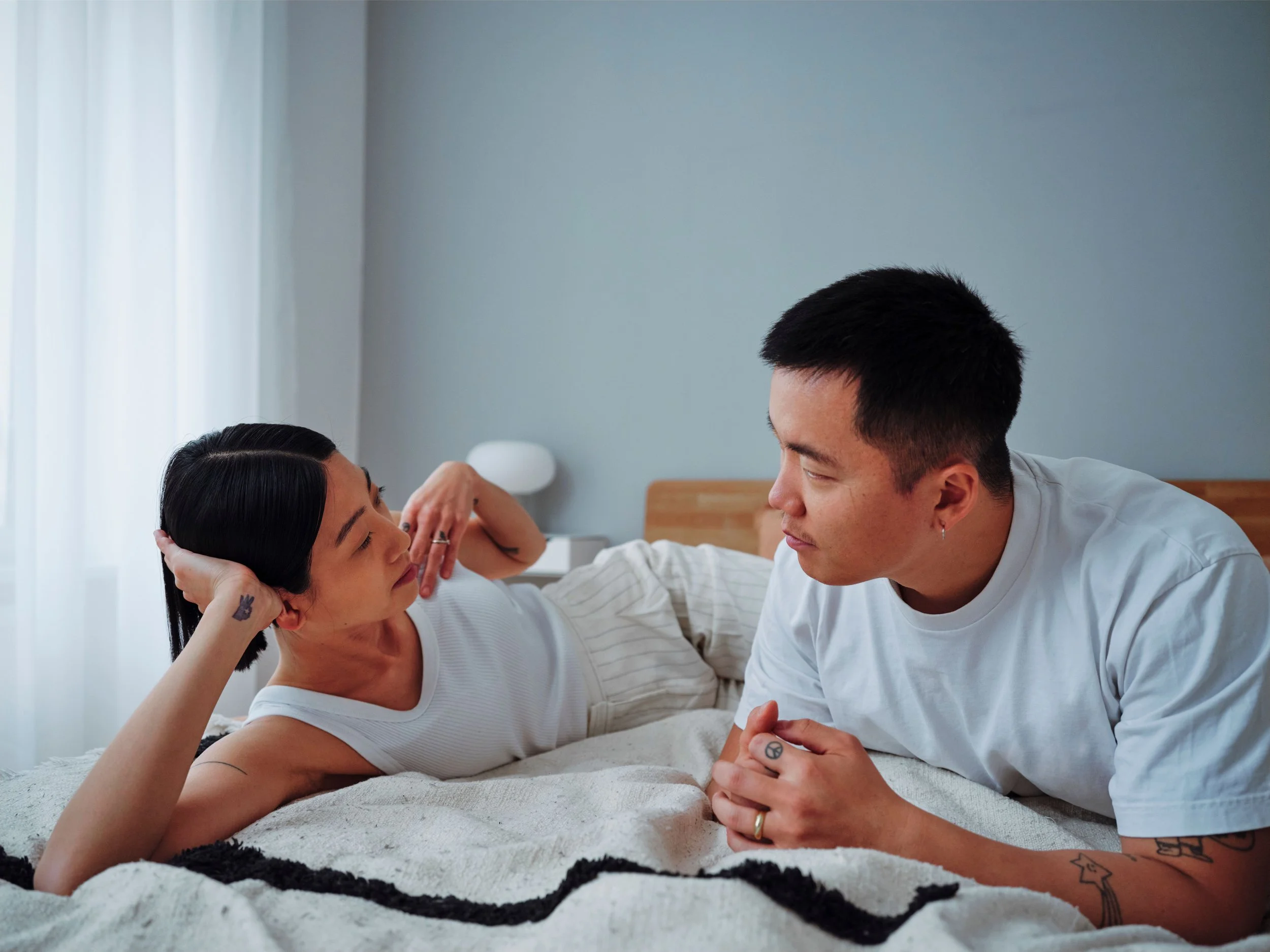 Couple lying in bed facing each other and having a conversation, reflecting the importance of understanding different perspectives in couples therapy.