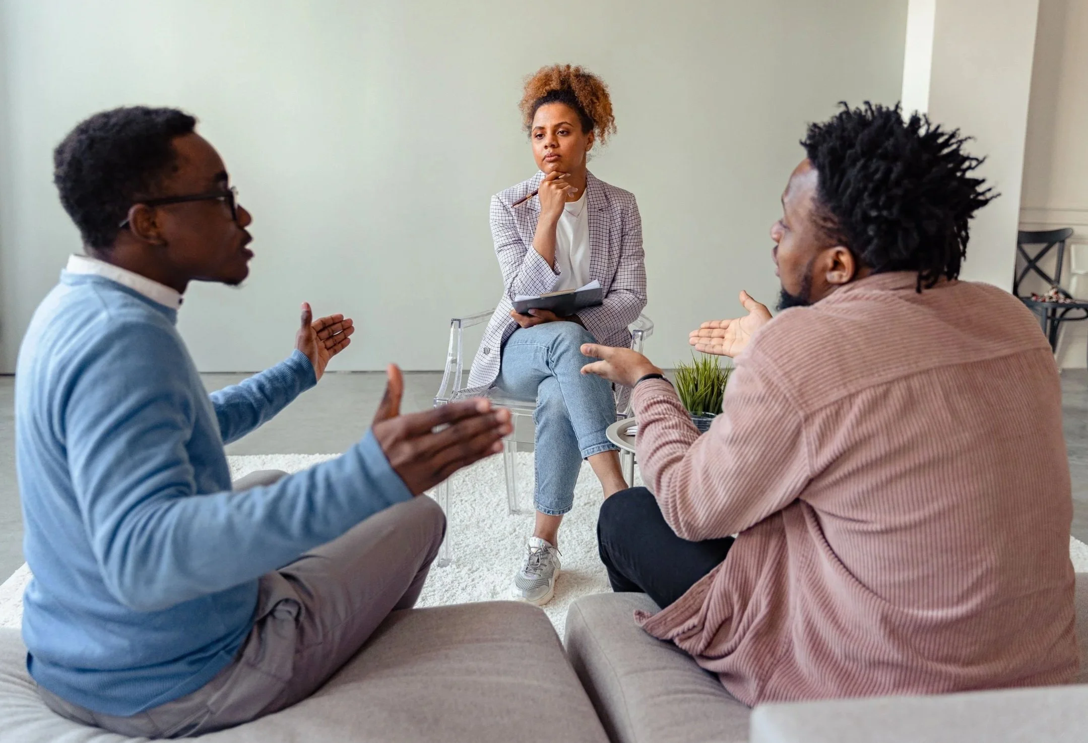 two men of color sitting facing each other talking with their hands with a woman of color therapist listening to them during a marriage counseling session in Worcester.